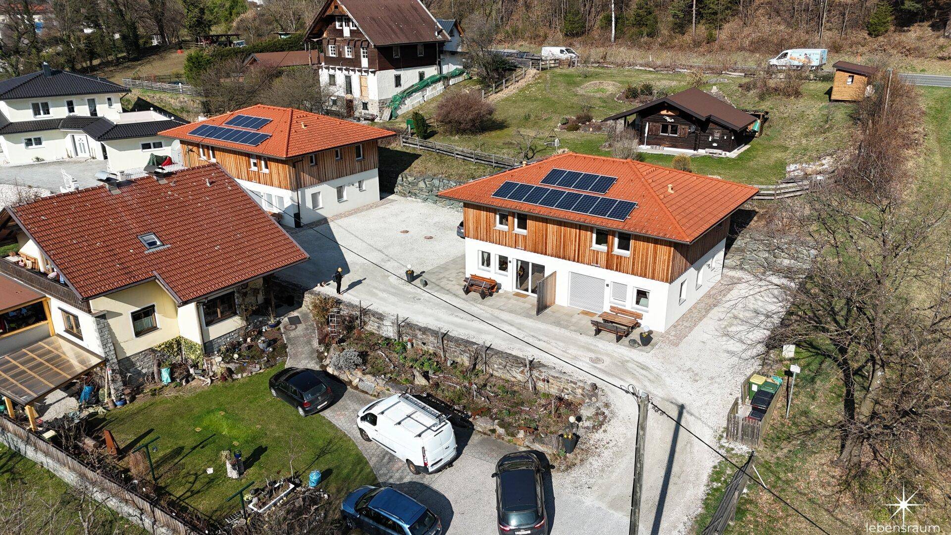 Panoramablick aus der Luft auf die Häusergruppe, umgeben von Natur und mit Solarpaneelen.