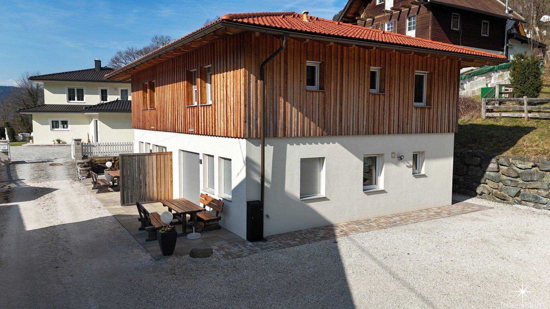 Ansicht des Hauses mit traditioneller Holzverkleidung und moderner Putzfassade in ländlicher Umgebung.