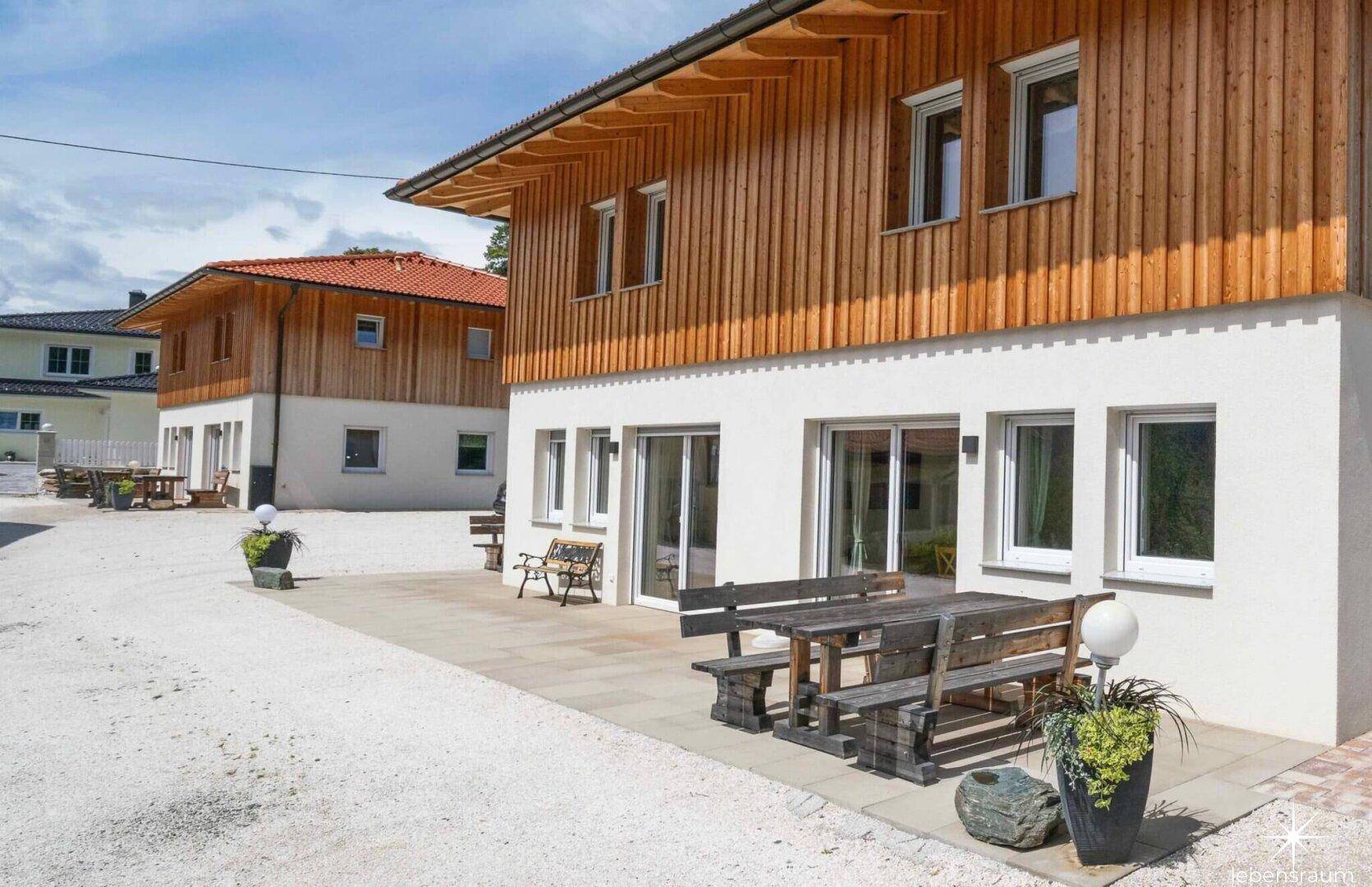 Vorderansicht des Hauses mit gepflasterter Terrasse und Holzbänken, bereit für den Außenbereich.