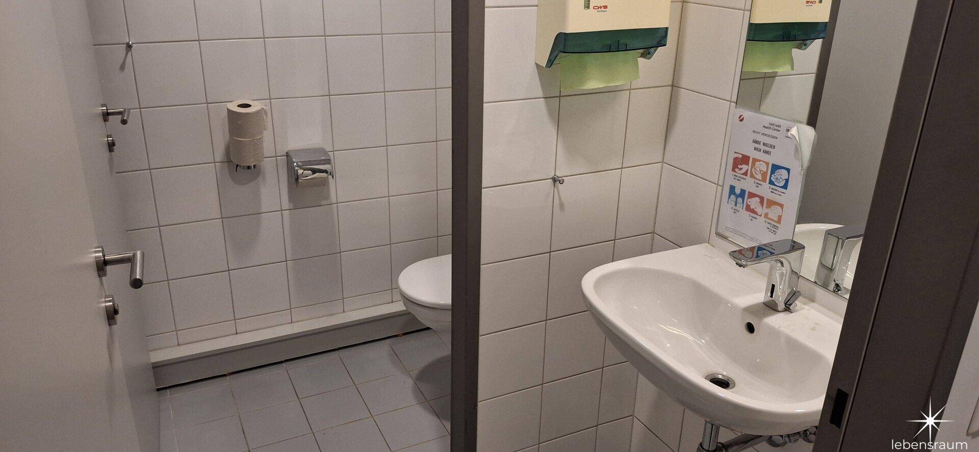 Saubere Toilette mit weißen Fliesen, Waschbecken und Spiegel, gut gepflegt.