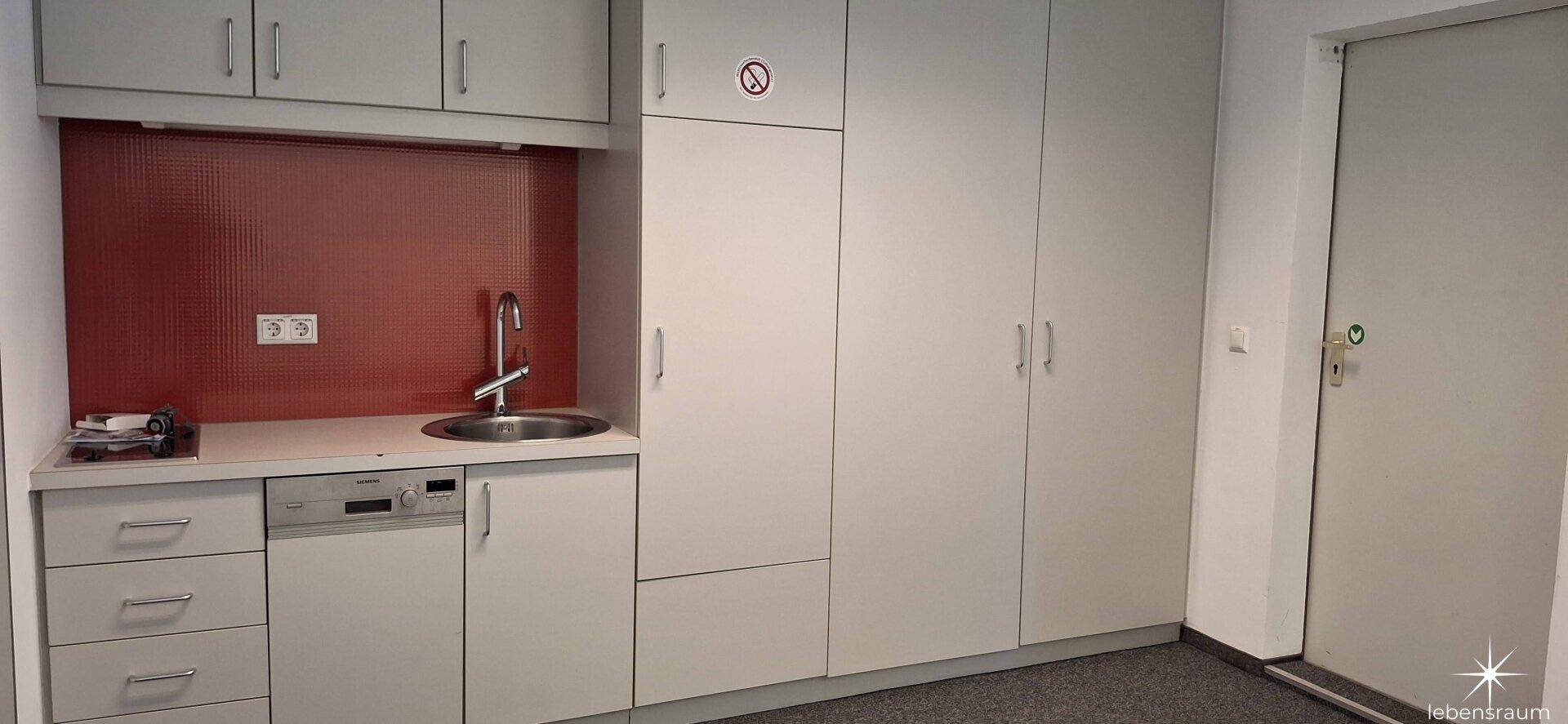 Moderne Küchenzeile mit weißen Schränken, Spülmaschine und roter Rückwand, ideal für Pausen.