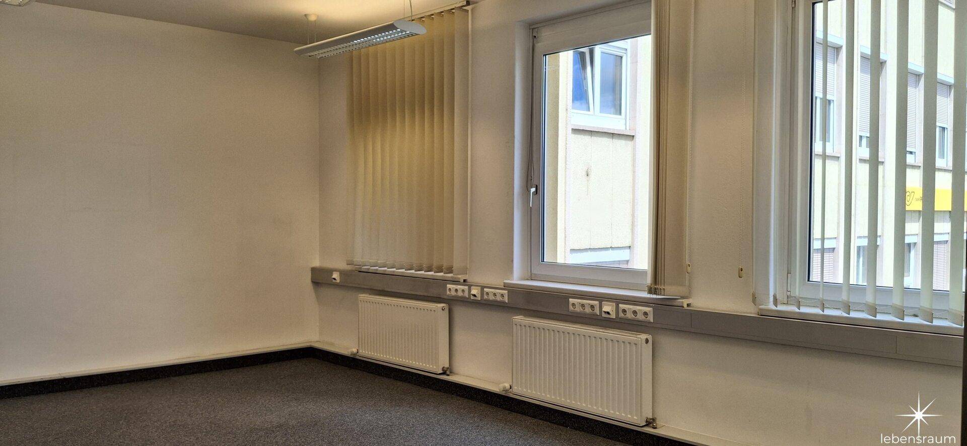 Büro mit mehreren Fenstern und Heizkörpern, bietet eine helle und funktionale Arbeitsumgebung.
