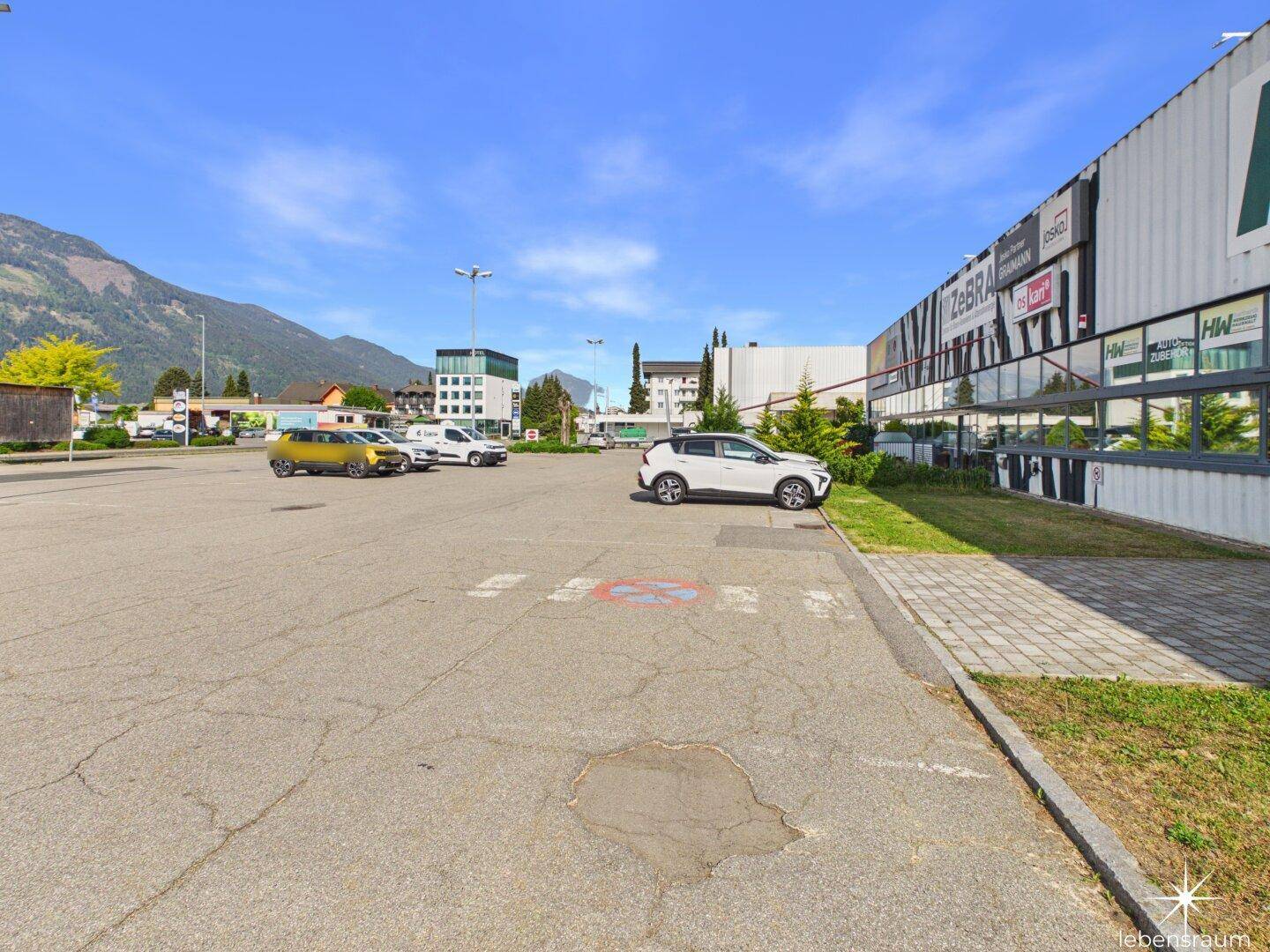 Großer Parkplatz vor dem Gewerbegebäude mit Blick auf die umliegende Berglandschaft.