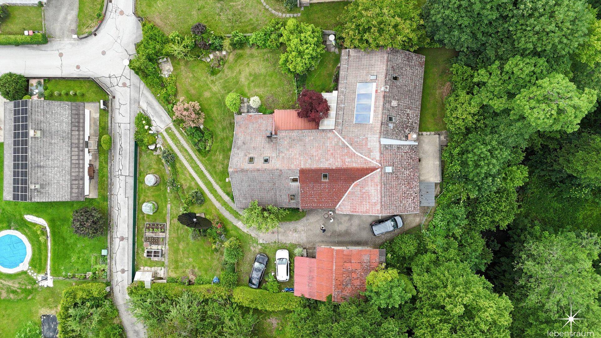 Luftaufnahme des Anwesens mit mehreren Gebäuden, viel Grünfläche und angrenzendem Wald.