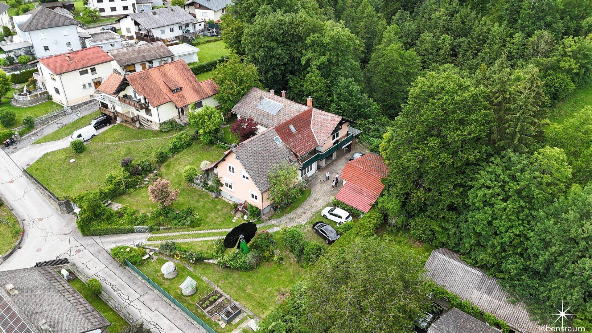Schrägansicht des Hauses und der umliegenden Nachbarschaft mit viel Grün und Wald im Hintergrund.