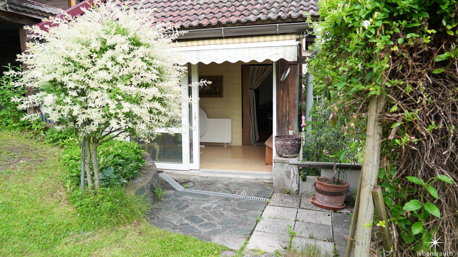 Kleiner Gartenbereich mit blühendem Baum und Zugang zu einem Zimmer mit Markise.