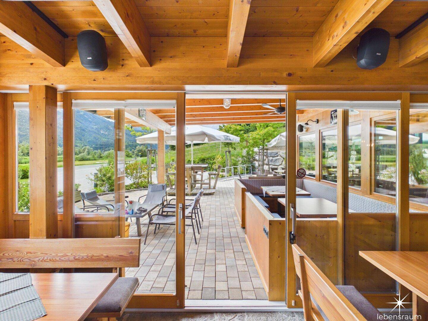Innenansicht eines Restaurants mit Blick auf die Außenterrasse und die umliegende Berglandschaft.