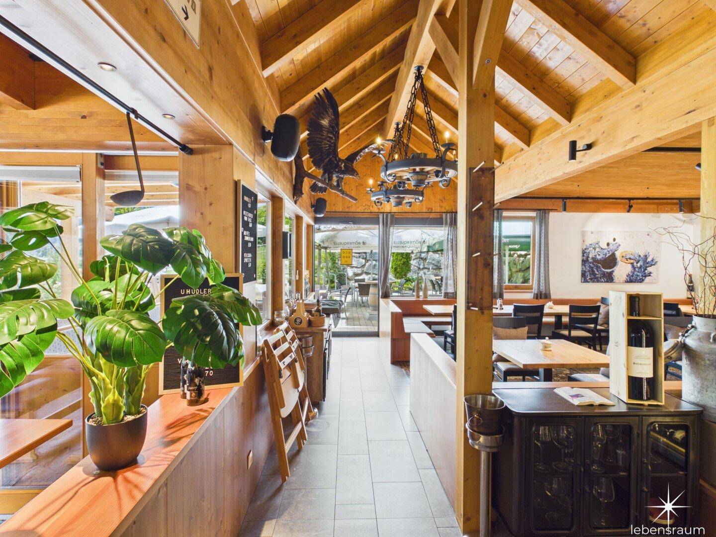 Langer Gang in einem Restaurant mit Holzbalkendecke, Fliesenboden und Blick auf die Terrasse.