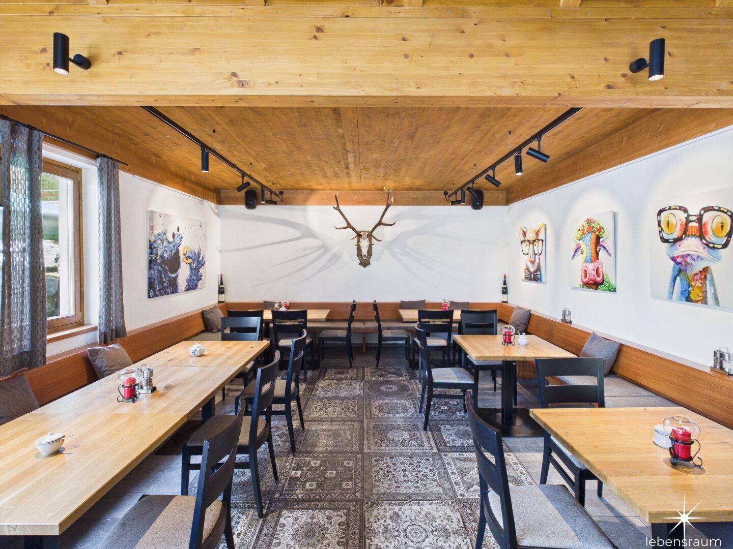 Großer Speisesaal mit Holzbalkendecke, gemustertem Teppich und Hirschgeweih an der Wand.
