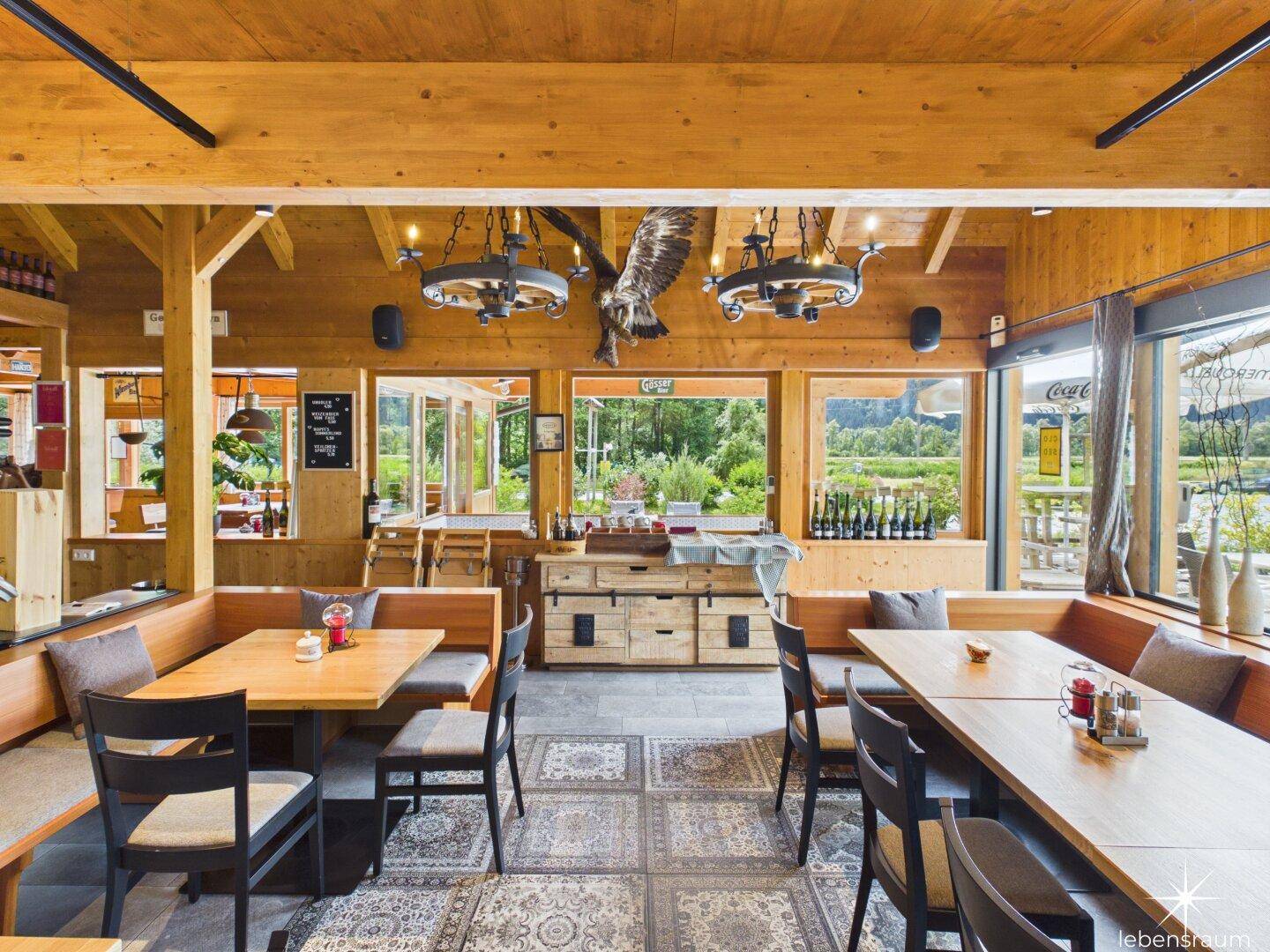 Restaurant mit Holzbalken, großen Fenstern und Blick auf die grüne Umgebung.