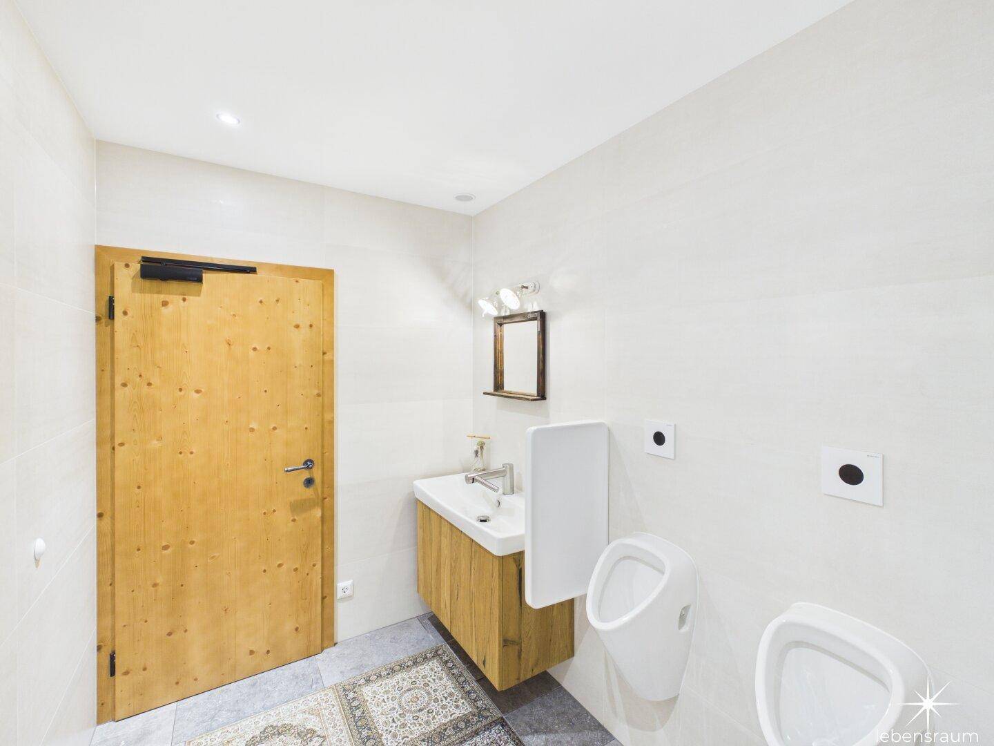 Modernes Gäste-WC mit weißen Fliesen, Holzwaschtisch und zwei Urinalen.