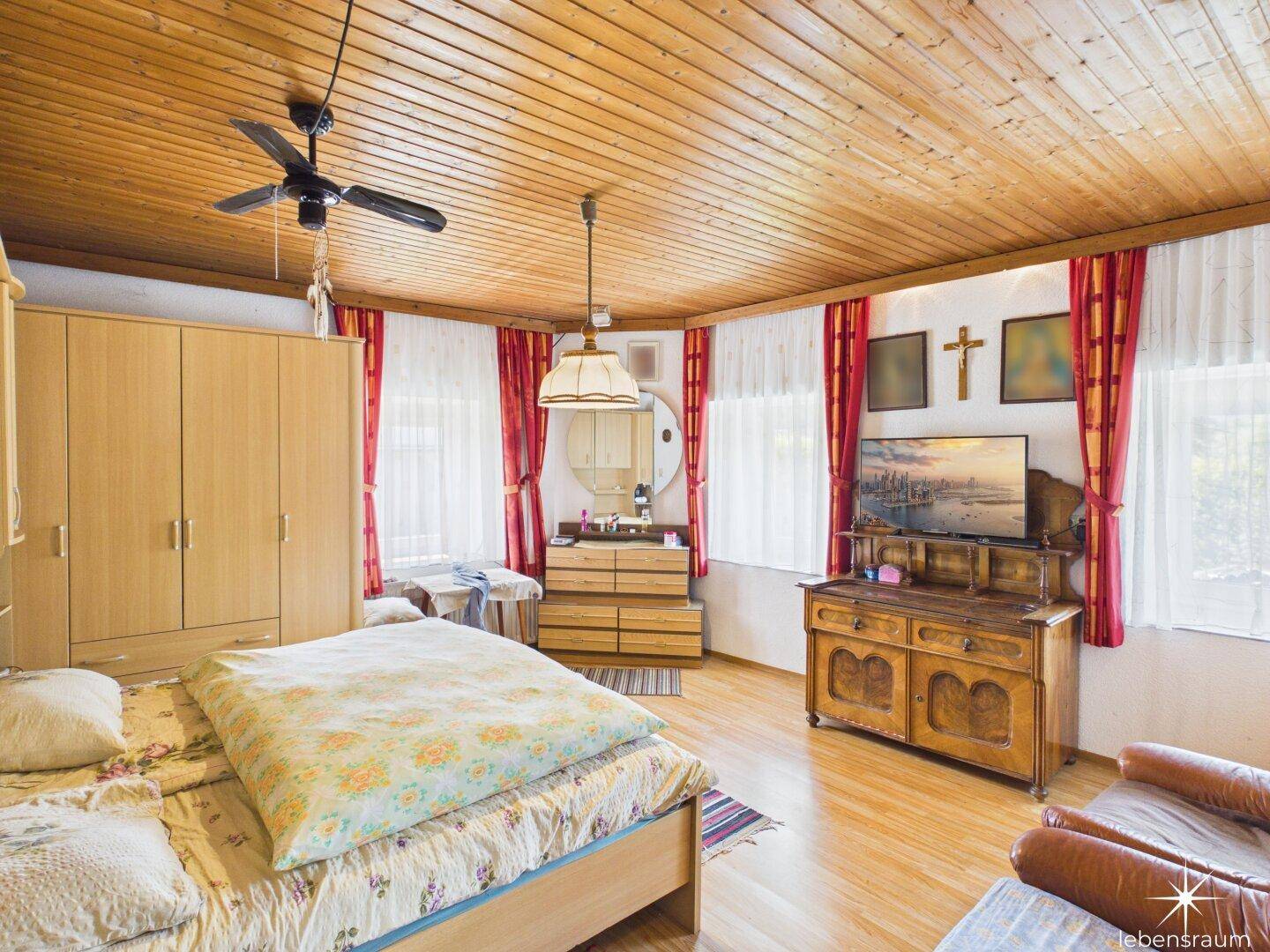 Schlafzimmer mit Holztäfelung an der Decke, Doppelbett und traditionellen Holzmöbeln.