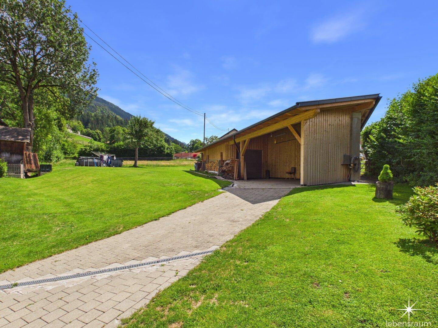 Großzügige Rasenfläche neben einem Holzschuppen mit Blick auf die Berge.