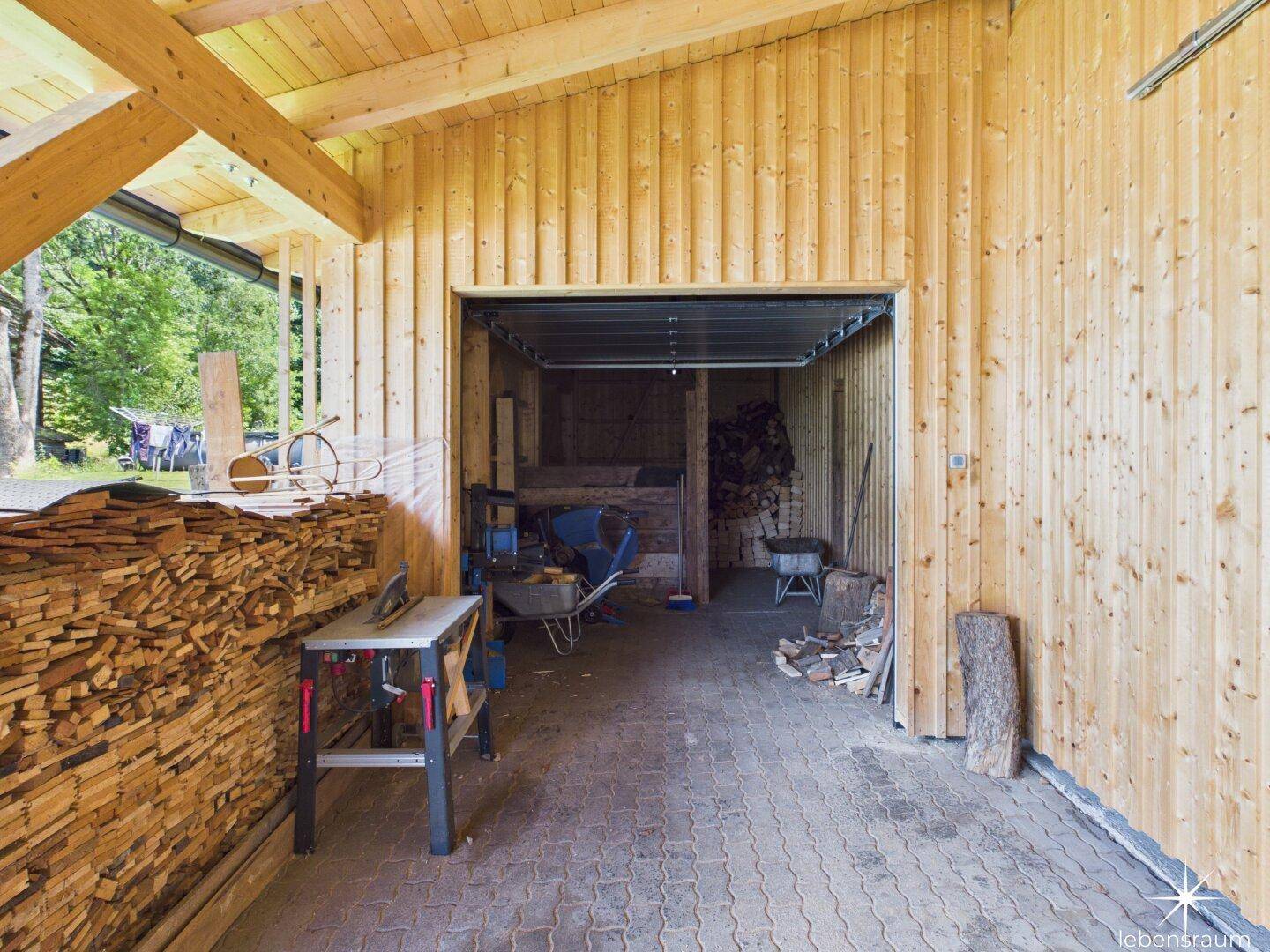 Innenansicht des Holzschuppens mit Lagerfläche, Werkbank und Holzlager.
