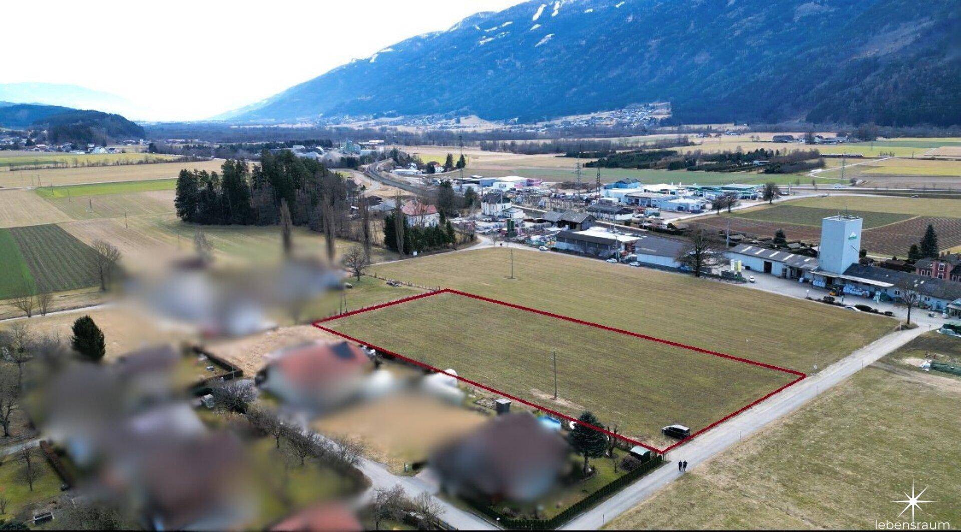Luftaufnahme eines großen Grundstücks, rot umrandet, umgeben von Feldern und Bergen.