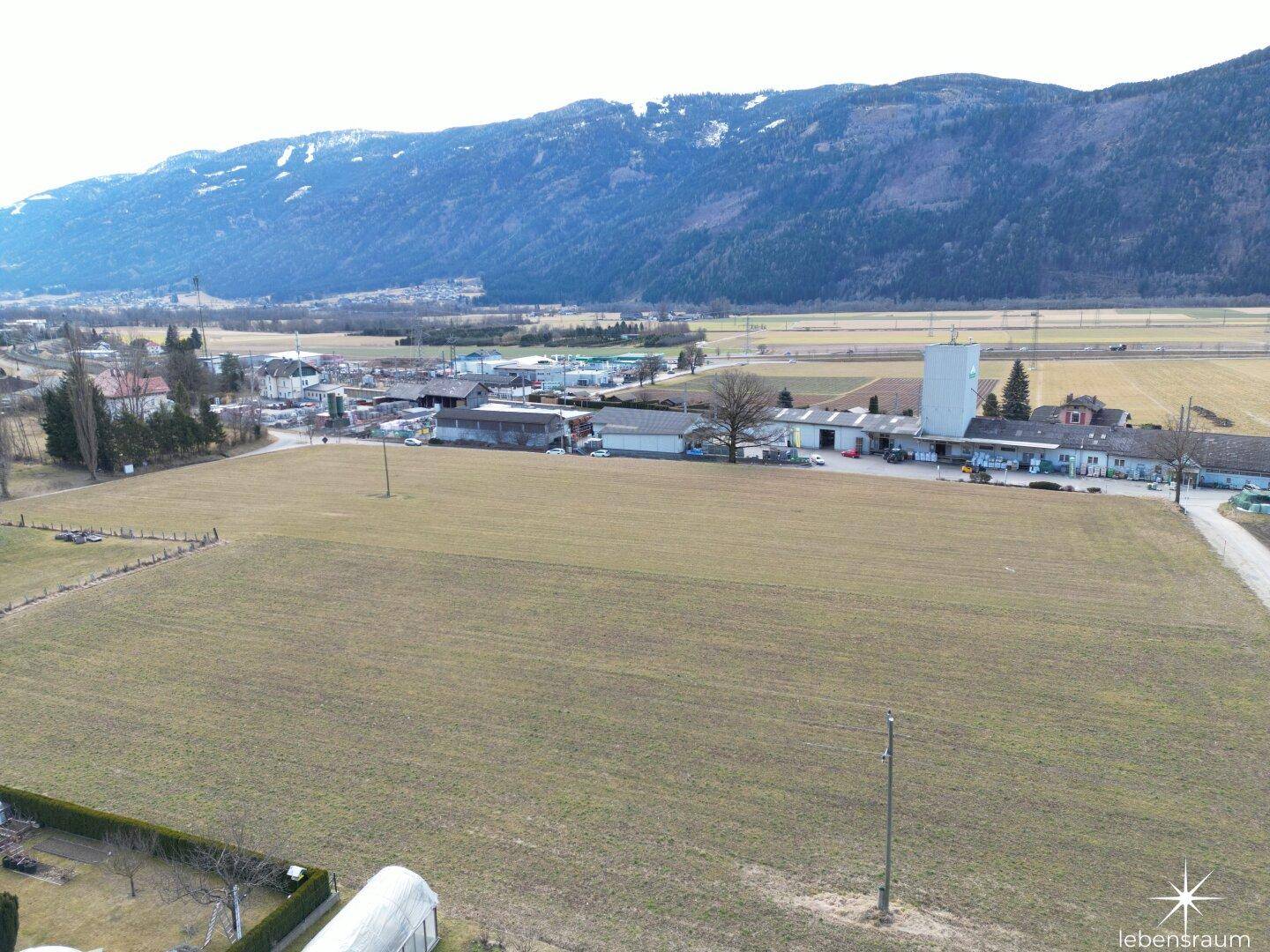Panoramablick aus der Luft auf weite Felder, ländliche Bebauung und majestätische Berge im Hintergrund.