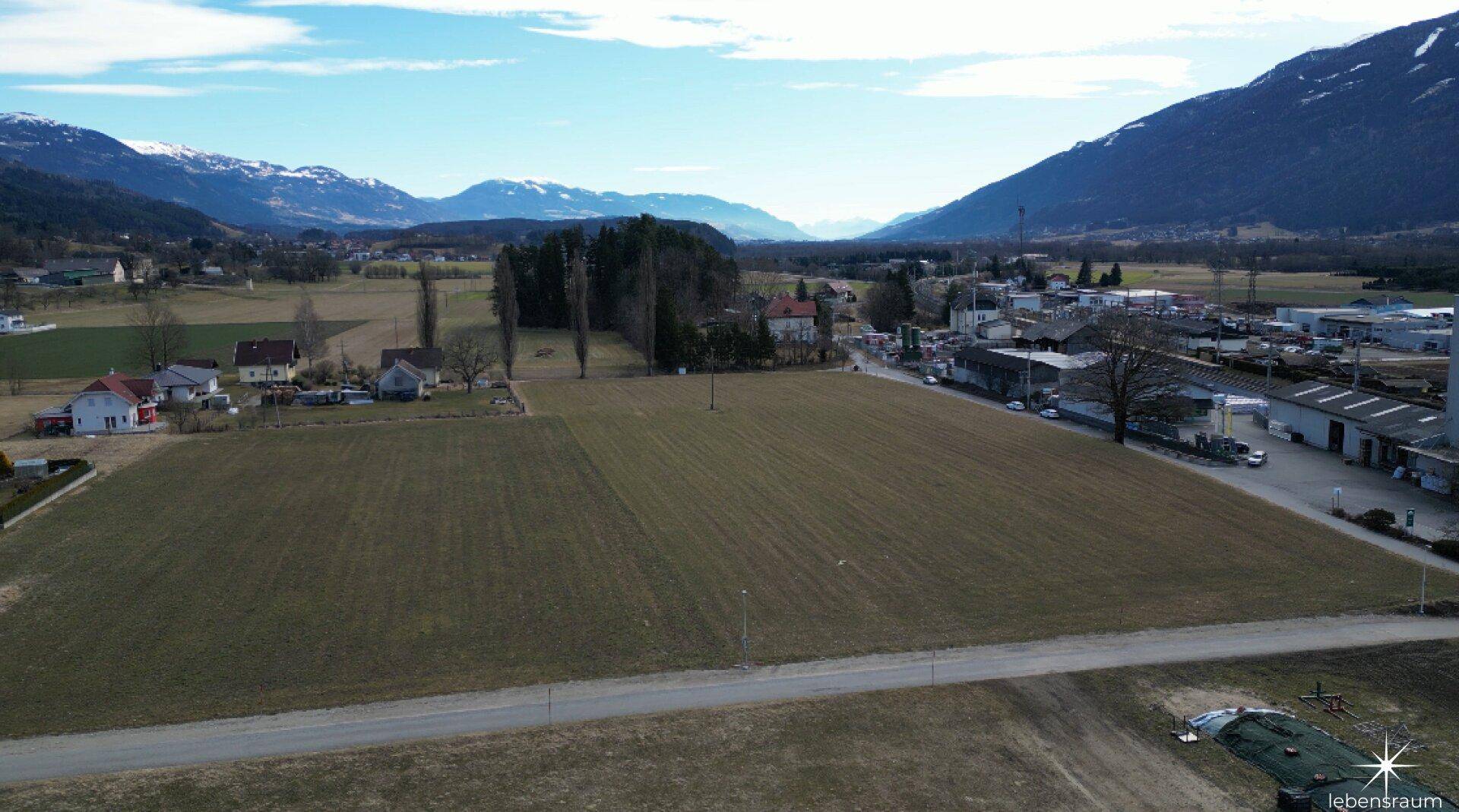 Luftaufnahme von weiten Feldern, einer Straße und ländlicher Bebauung mit Bergblick.