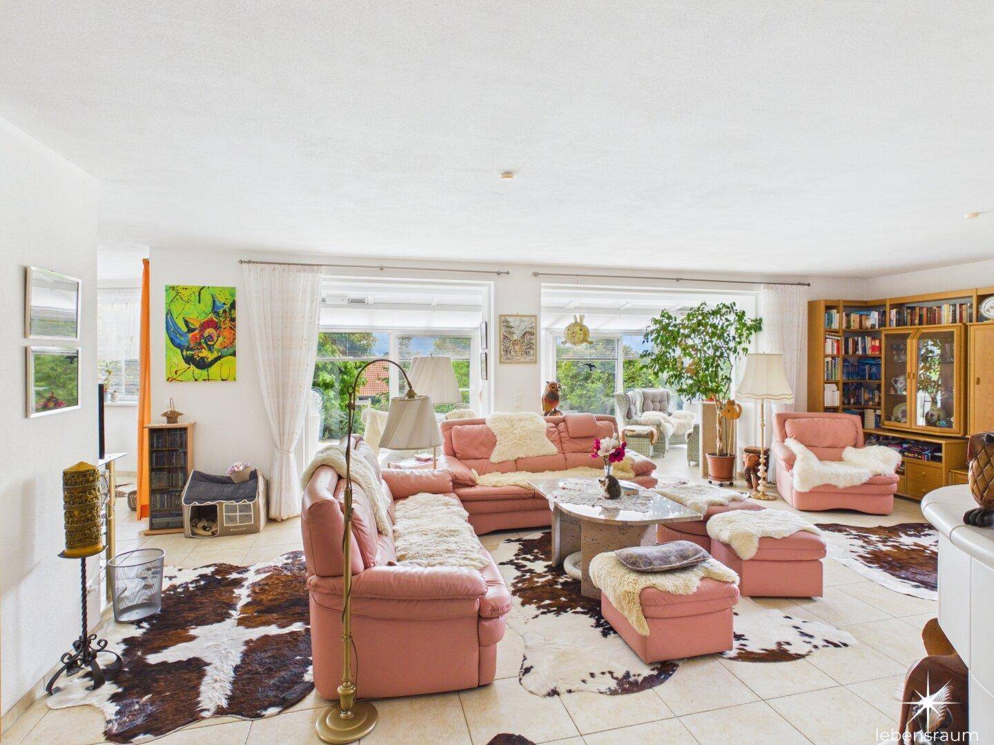 Gemütliches Wohnzimmer mit rosa Sofas, Tierfellteppichen und Blick ins Grüne.