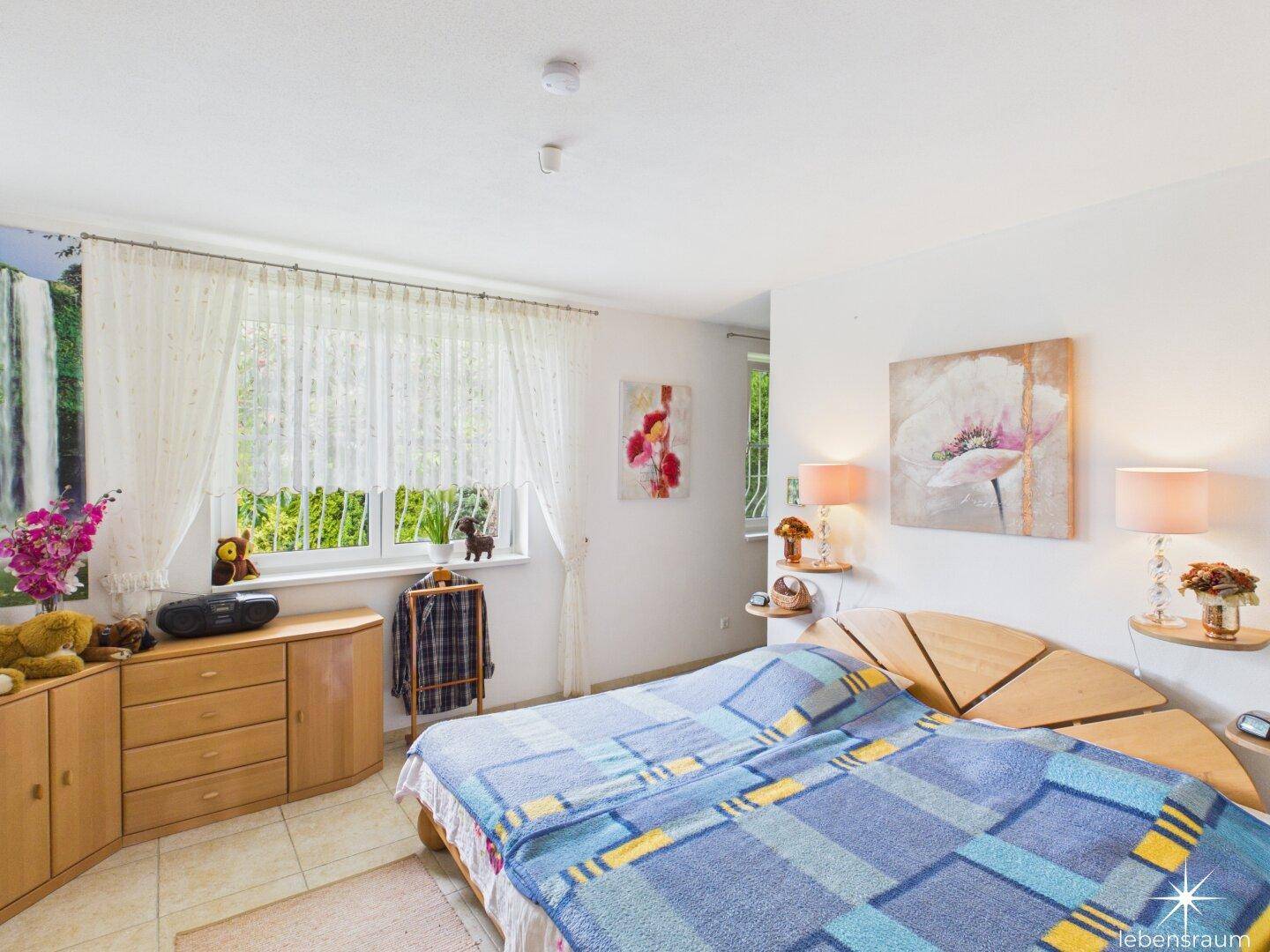Schlafzimmer mit Doppelbett, Holzmöbeln und einem Fenster mit Blick ins Grüne.