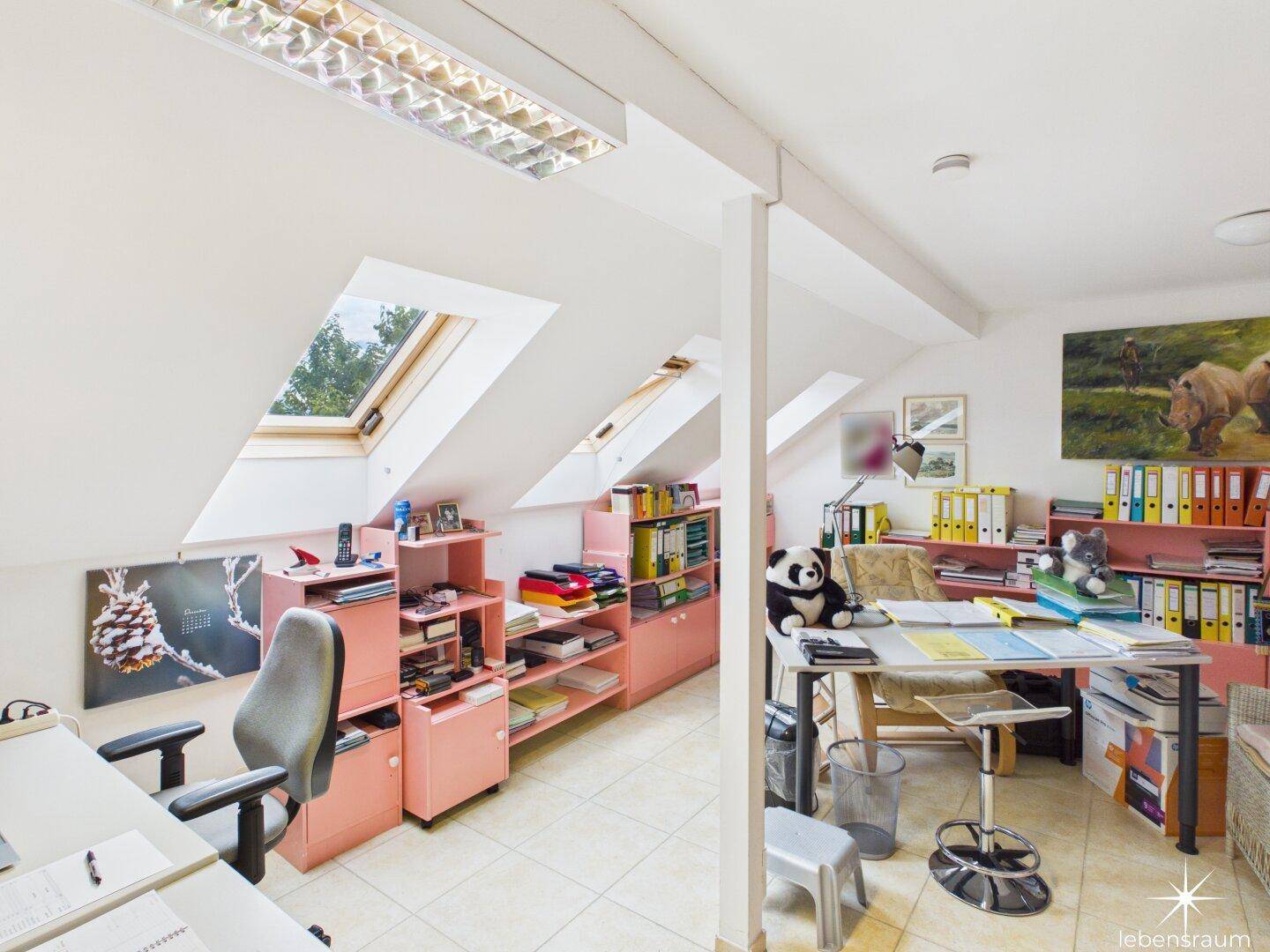 Dachgeschossbüro mit Schreibtischen, Regalen und Dachfenstern für natürliches Licht.