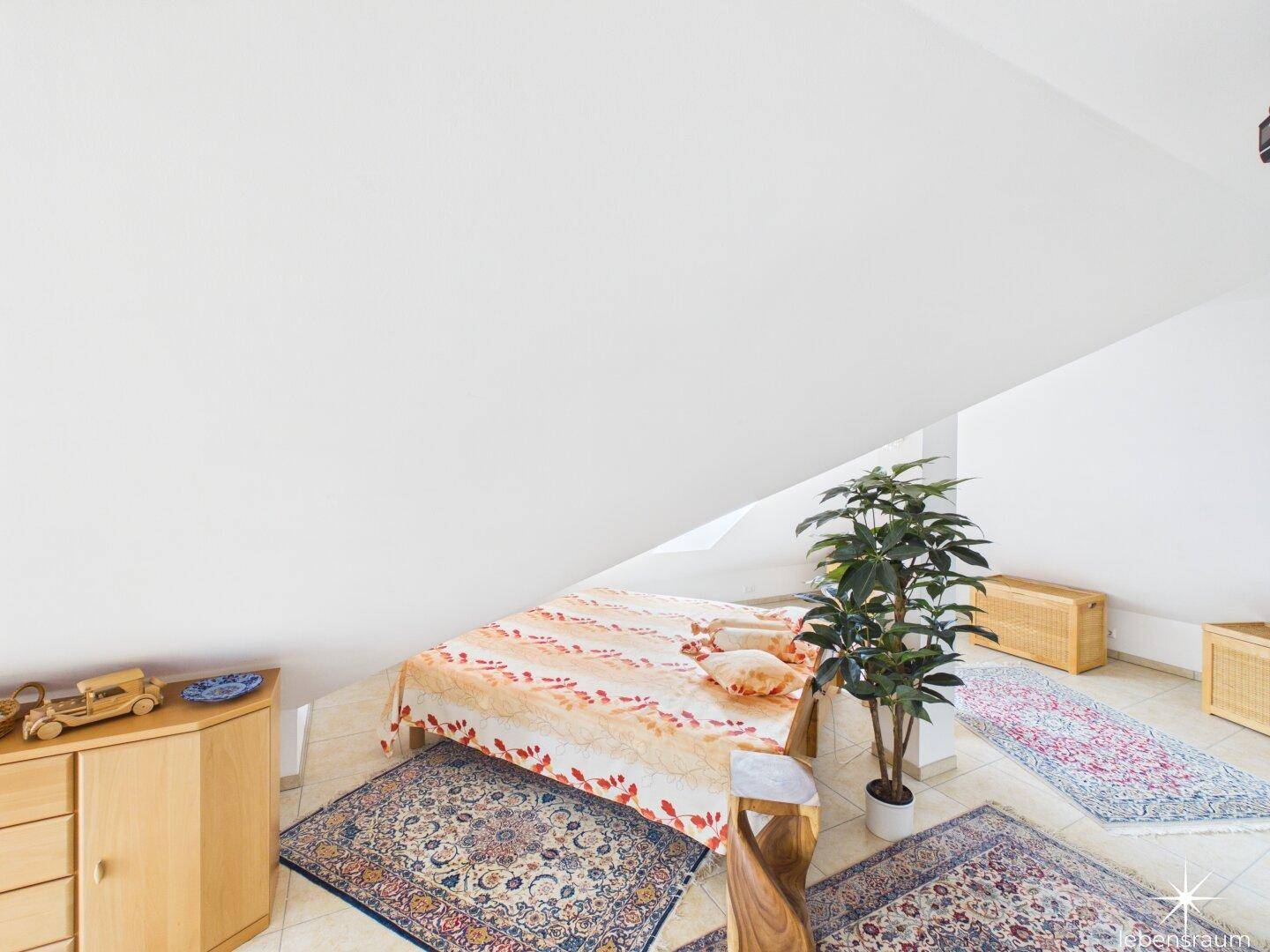 Schlafzimmer im Dachgeschoss mit schrägen Wänden, Doppelbett und Teppichen.