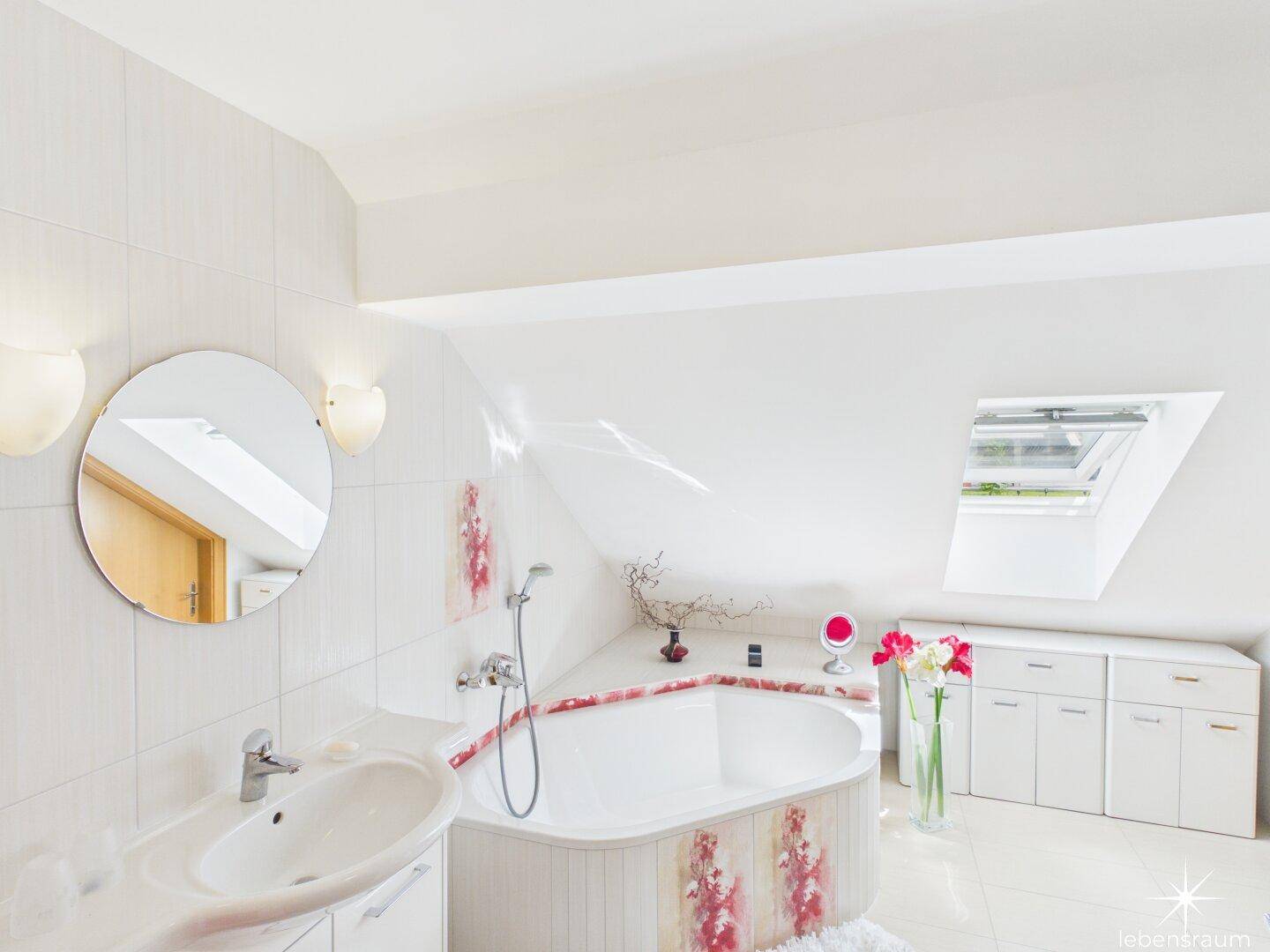 Modernes Badezimmer im Dachgeschoss mit Eckbadewanne, Waschbecken und Dachfenster.