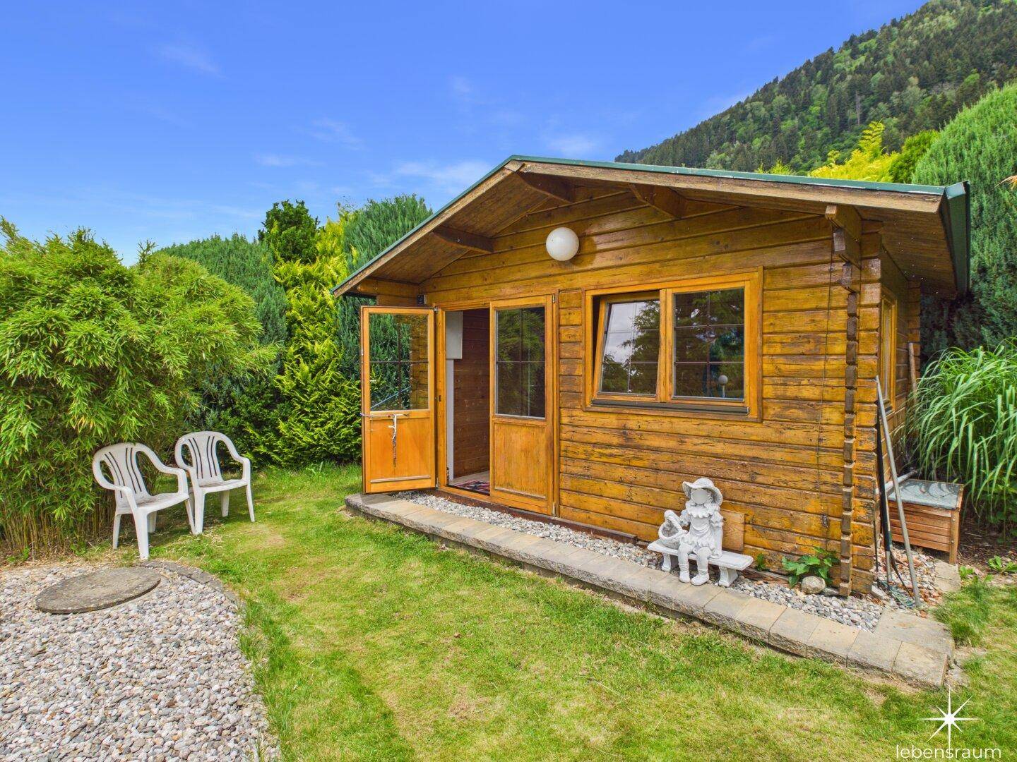 Rustikales Gartenhaus aus Holz mit geöffneter Tür, umgeben von Grünflächen.