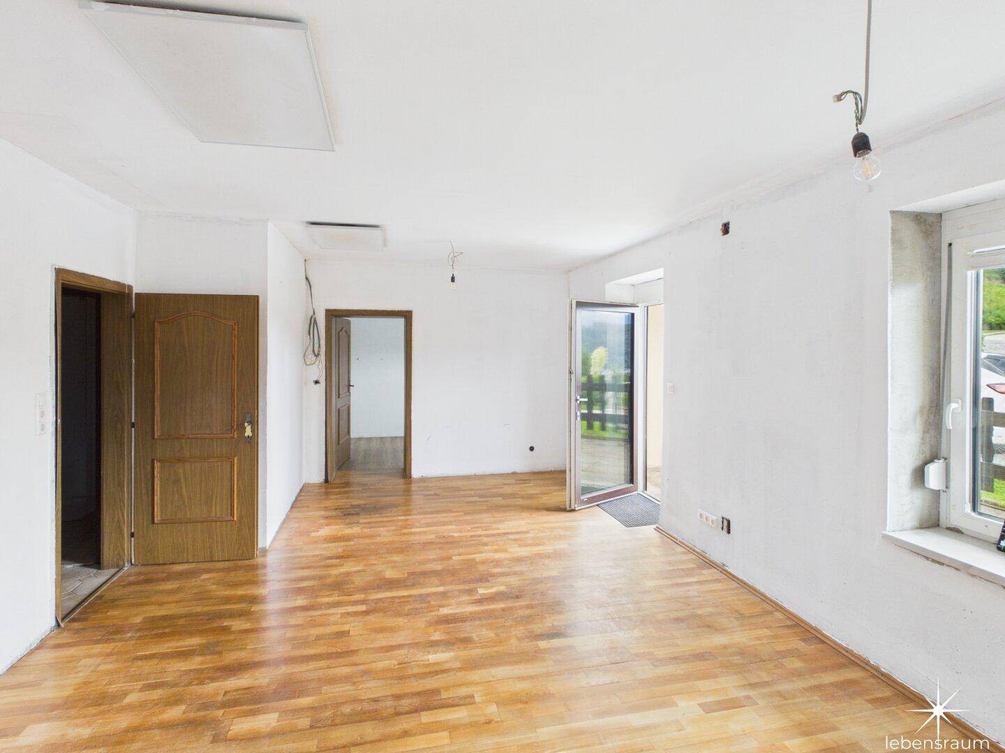 Heller, leerer Raum mit Holzboden und Zugang zu einem Balkon oder einer Terrasse.