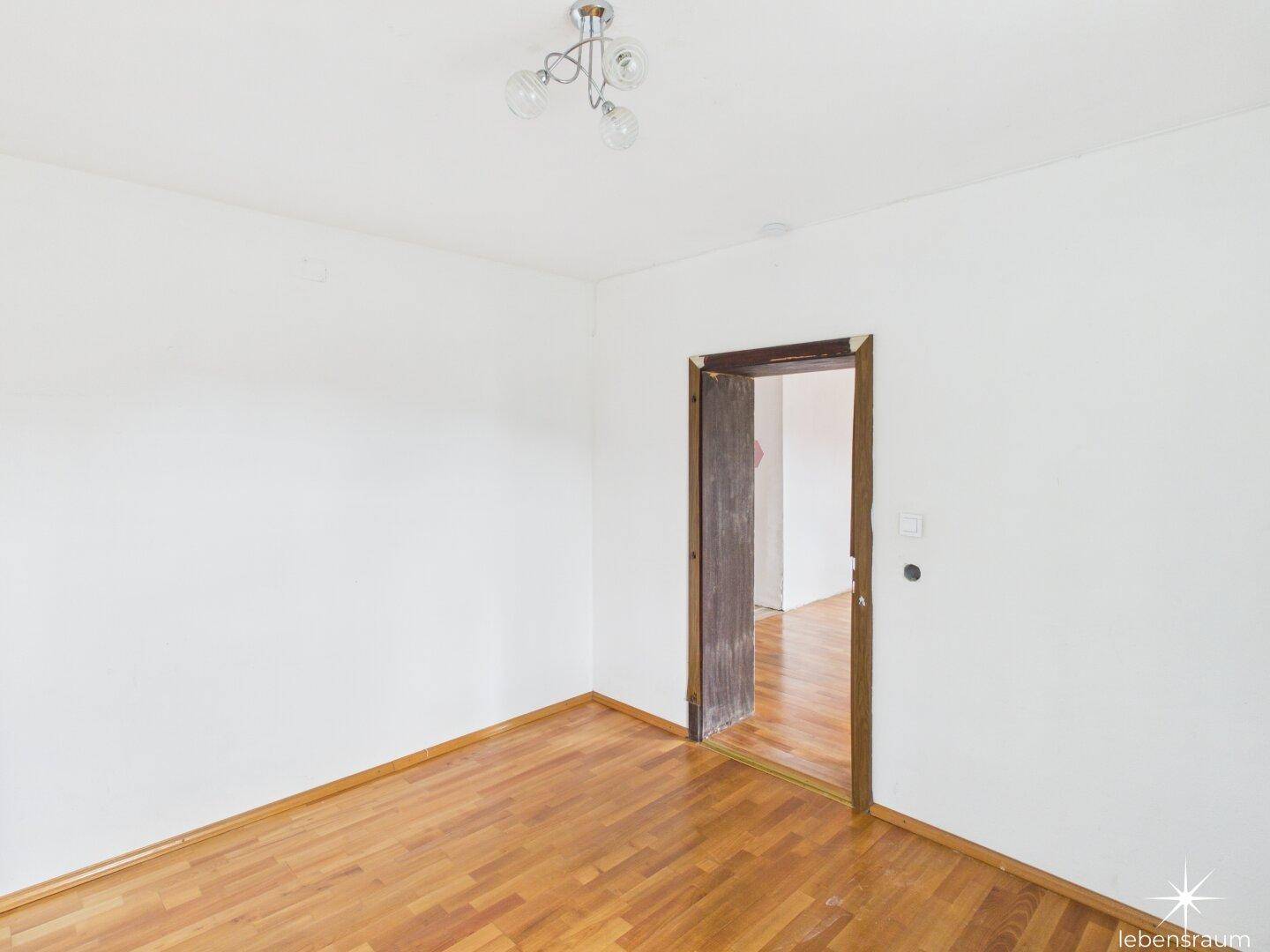 Leeres Zimmer mit Holzboden und einfacher Deckenleuchte, bereit zur individuellen Gestaltung.