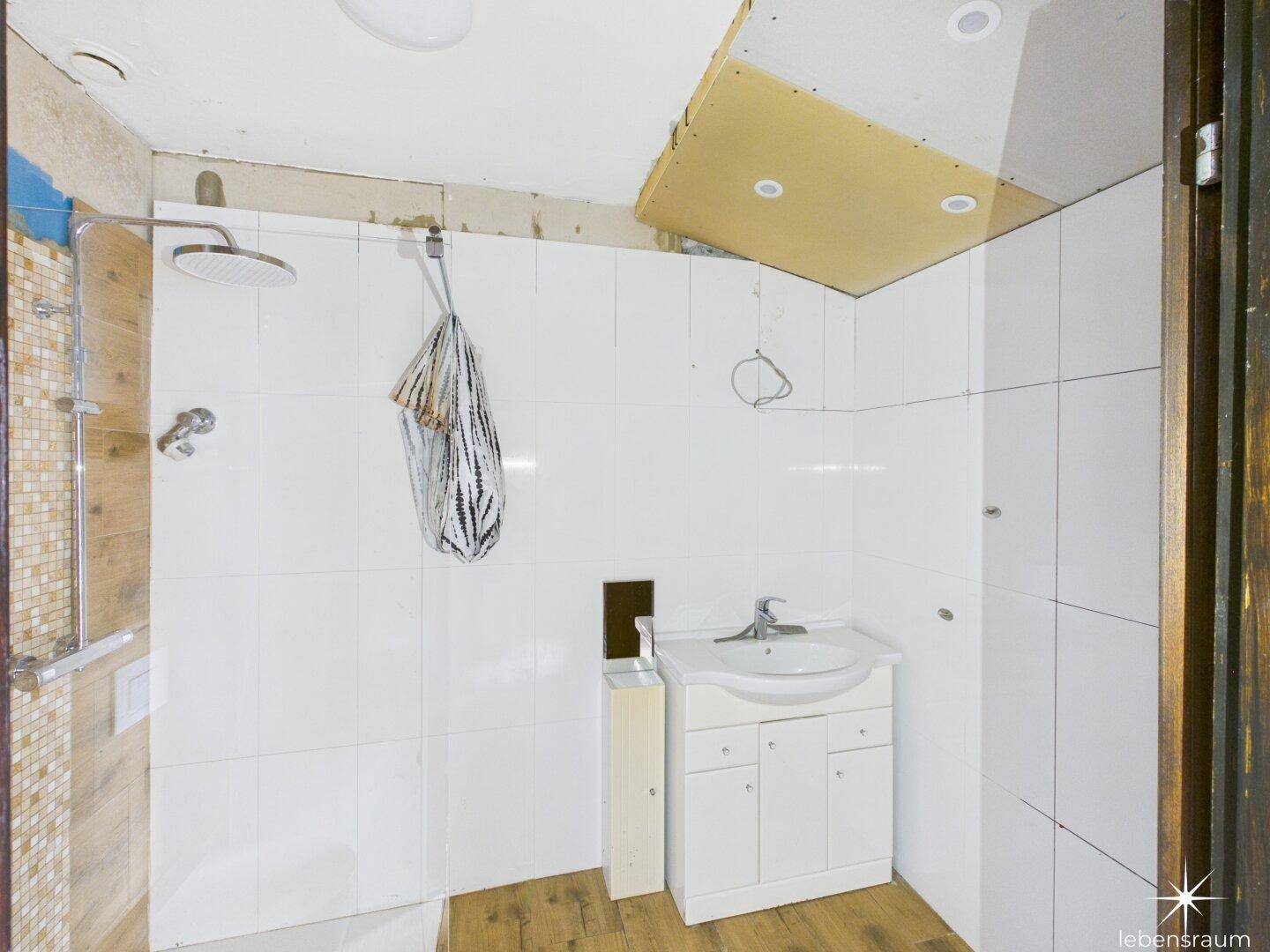 Badezimmer in Renovierung mit weiß gefliesten Wänden, Dusche und Waschbecken.