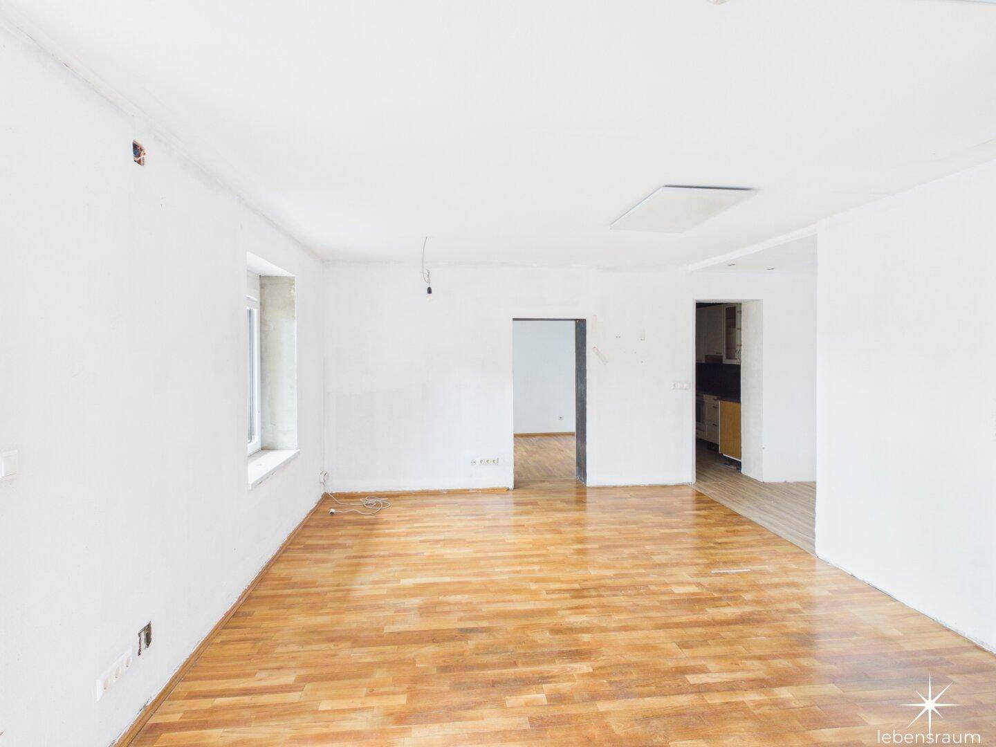 Großer, heller Wohnbereich mit Holzboden und mehreren Türen, ideal für offenes Wohnen.