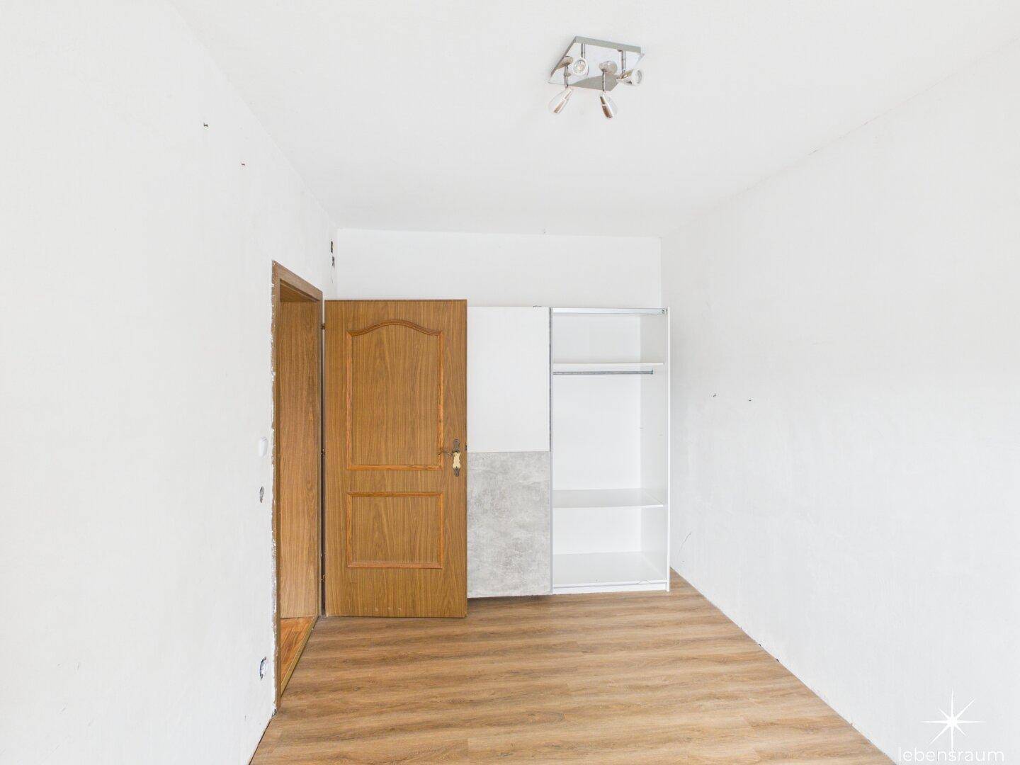 Unmöbliertes Zimmer mit Laminatboden und einem einfachen Kleiderschrank.