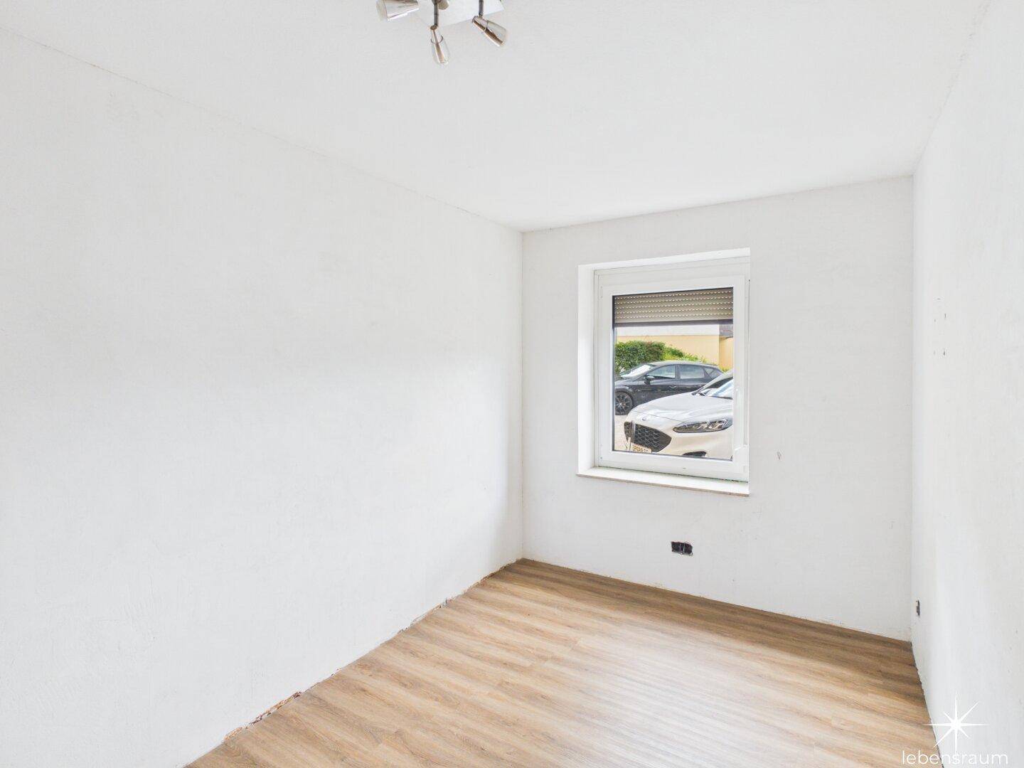 Helles, leeres Schlafzimmer mit Fenster und Blick auf geparkte Autos.