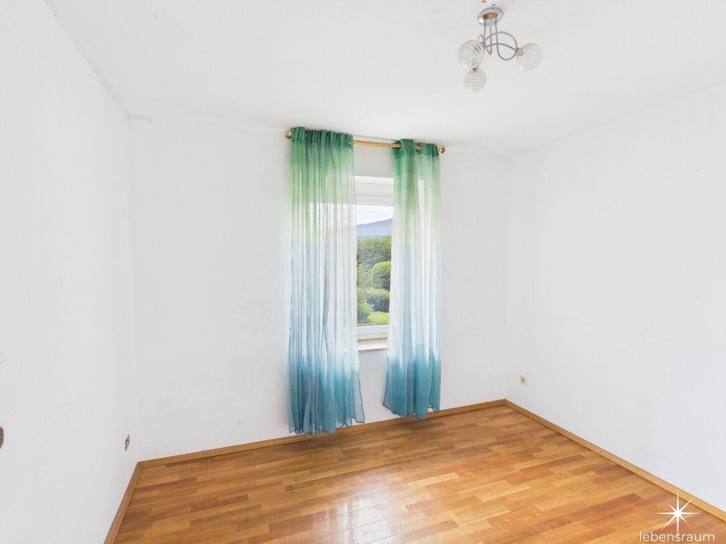 Helles Schlafzimmer mit Holzboden und Vorhängen, bietet einen grünen Ausblick.