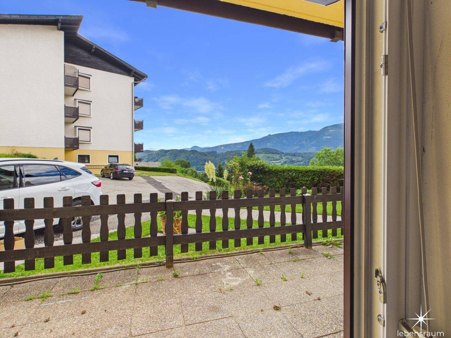 Blick von der Terrasse auf die umliegende Landschaft und Berge unter blauem Himmel.