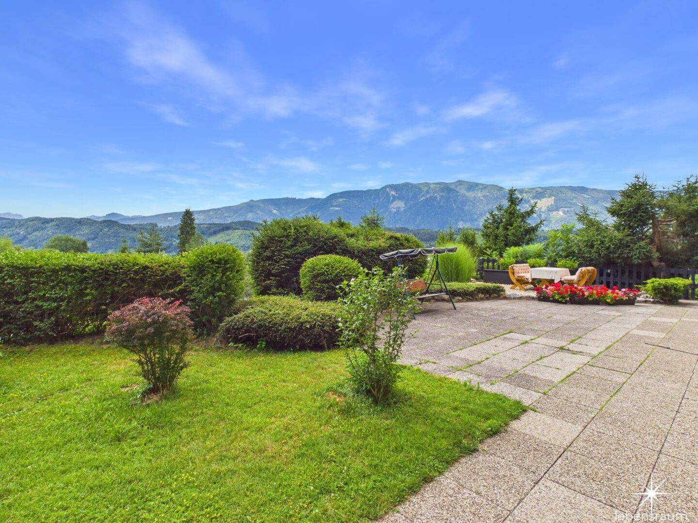 Großzügige Terrasse mit Rasenfläche, Hecken und weitem Bergblick, ideal zum Entspannen.