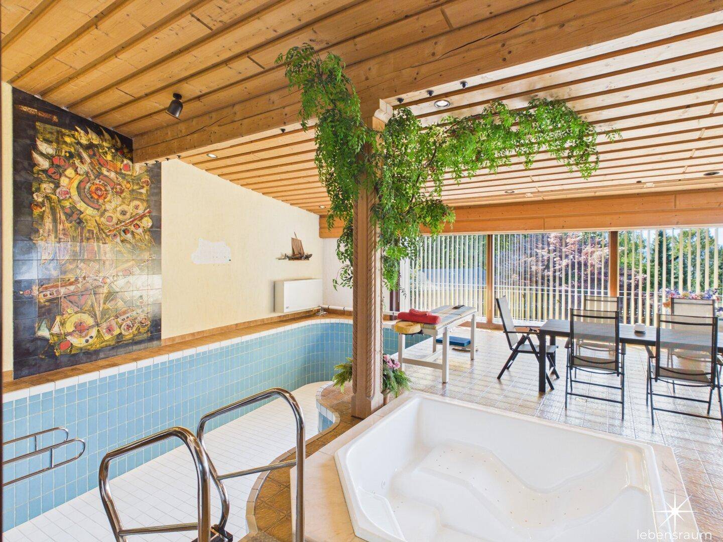 Innenpoolbereich mit Whirlpool, Holzdecke und großen Fenstern mit Blick ins Grüne.