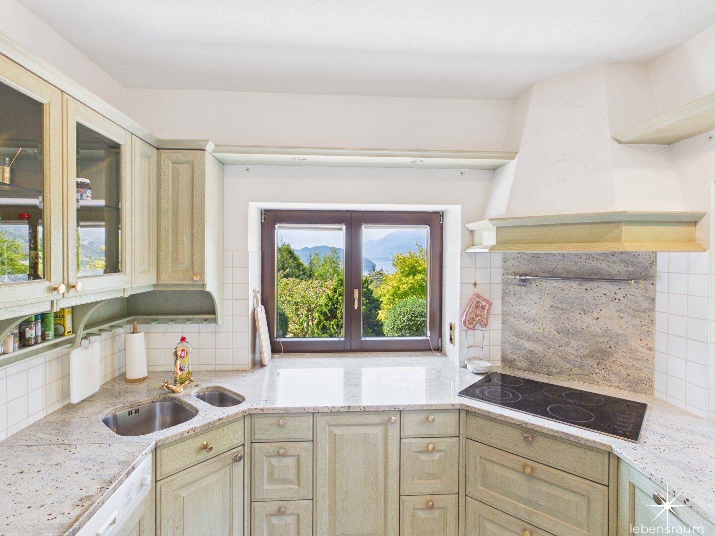 Traditionelle Küche mit hellgrünen Schränken, Granitarbeitsplatte und Fenster mit Blick ins Grüne.