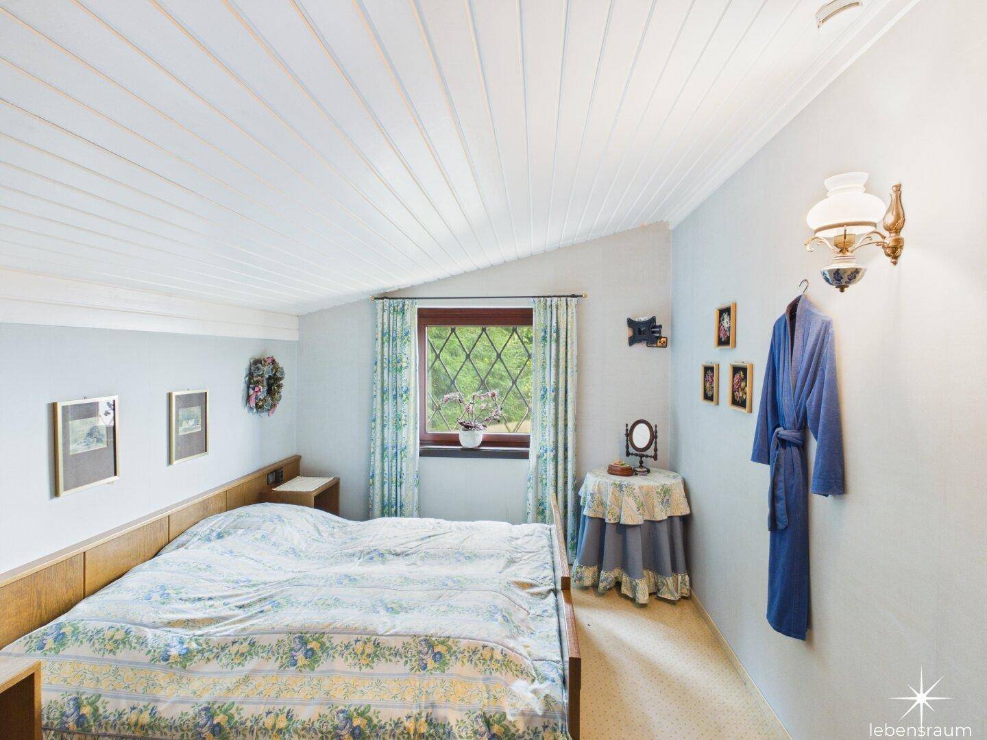 Schlafzimmer mit weißer Holzdecke, hellblauen Wänden und Fenster mit Blick ins Grüne.
