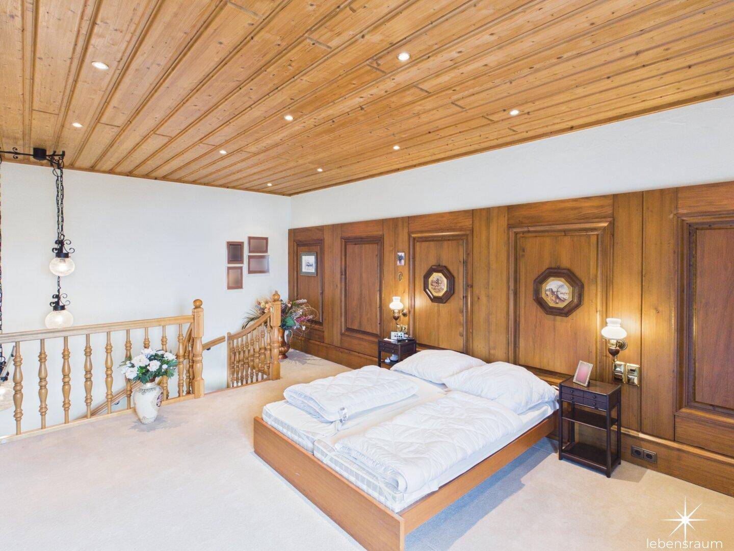Schlafzimmer mit Holzwänden, Holzdecke und Teppichboden, offen zum Treppenbereich.
