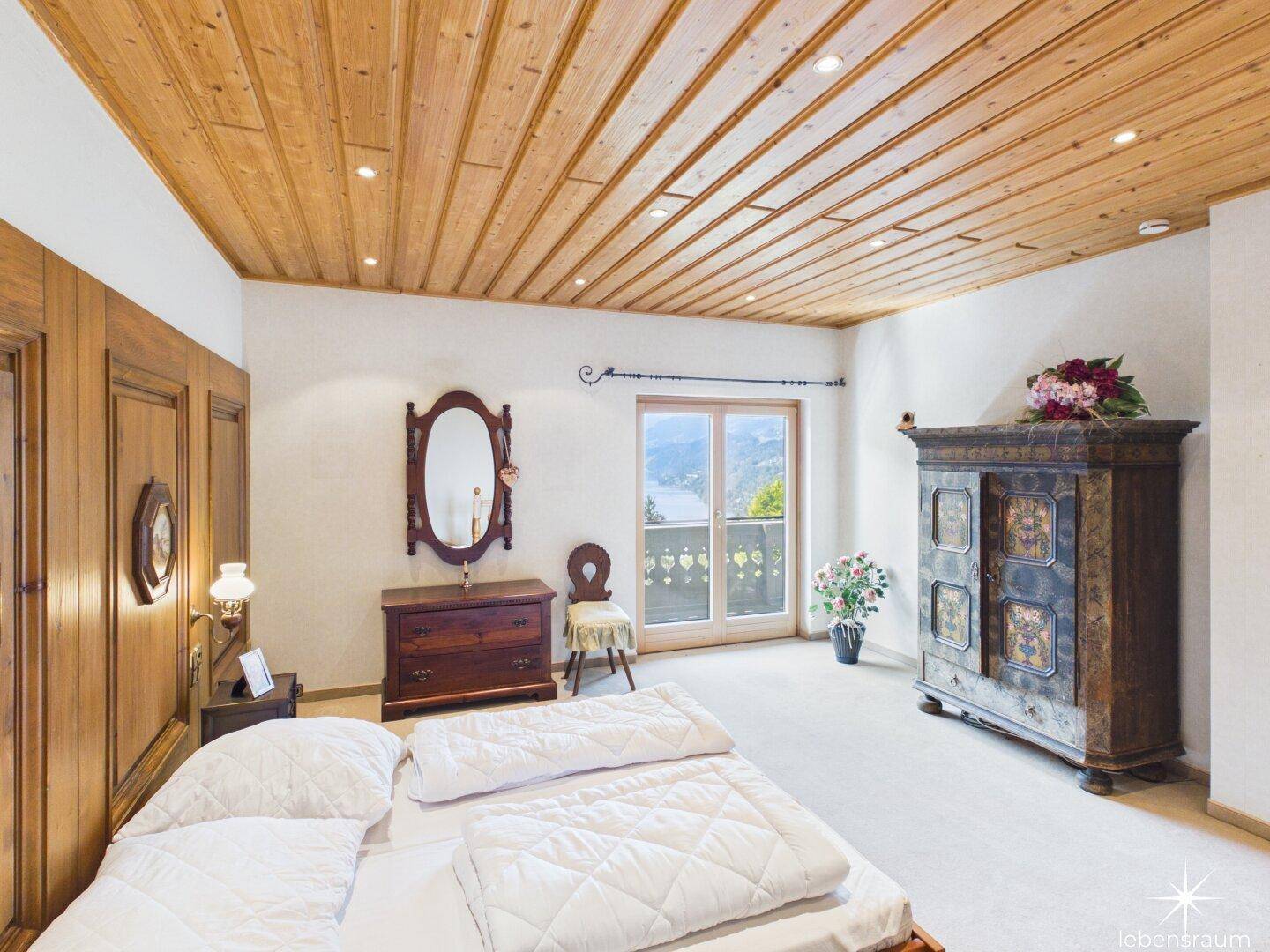 Traditionelles Schlafzimmer mit Holzelementen, antiken Möbeln und Balkonzugang mit Seeblick.