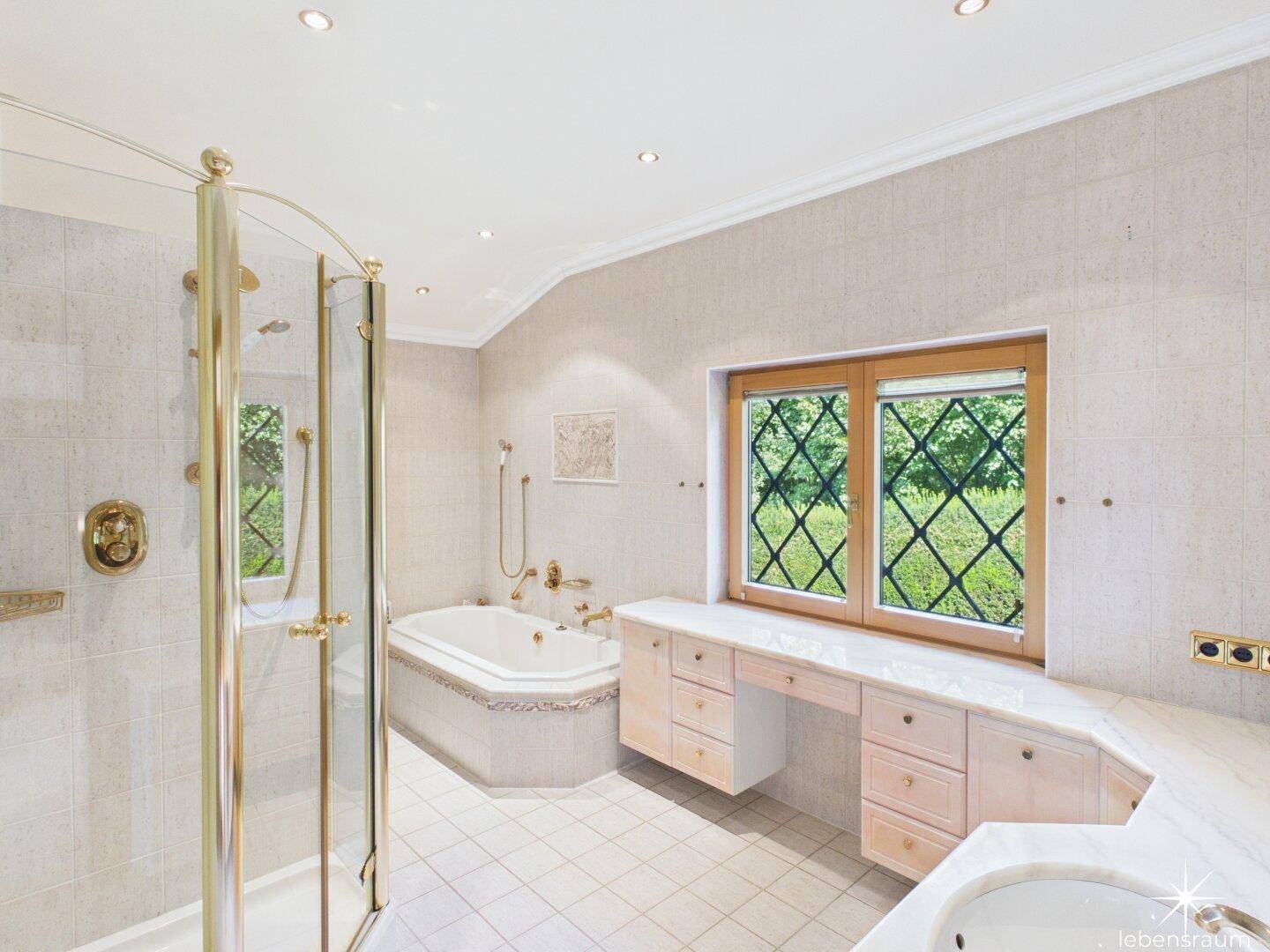 Helles Badezimmer mit Dusche, Eckbadewanne, Doppelwaschbecken und Fenster mit Blick ins Grüne.