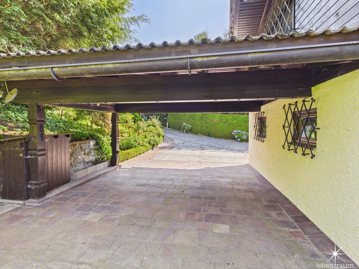 Überdachter Carport-Bereich mit gepflastertem Boden und Blick auf die Auffahrt.