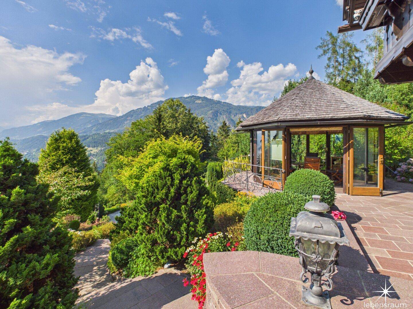 Eleganter Pavillon auf einer Terrasse, umgeben von Grün, mit Bergblick in der Ferne.