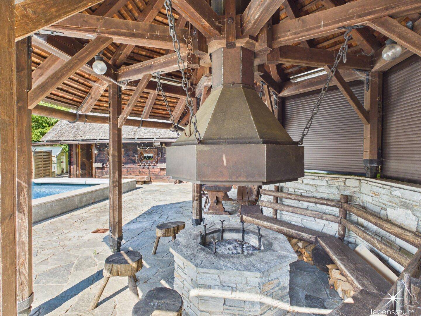 Überdachter Außenkamin mit Steinsitzgelegenheiten und Holzkonstruktion, ideal für gesellige Abende.
