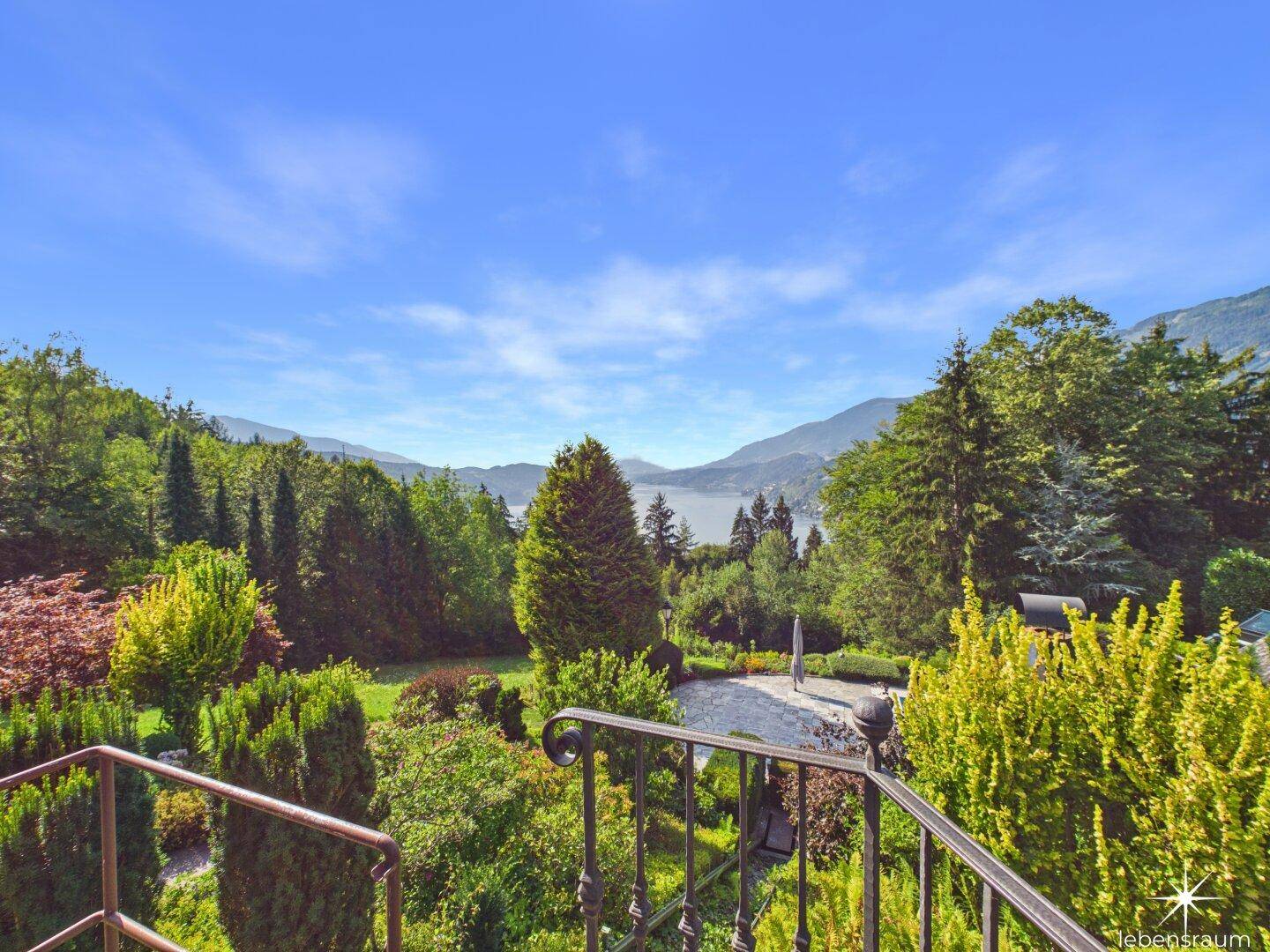 Panoramablick von einem Balkon auf einen See und die umliegende Berglandschaft mit üppiger Vegetation.