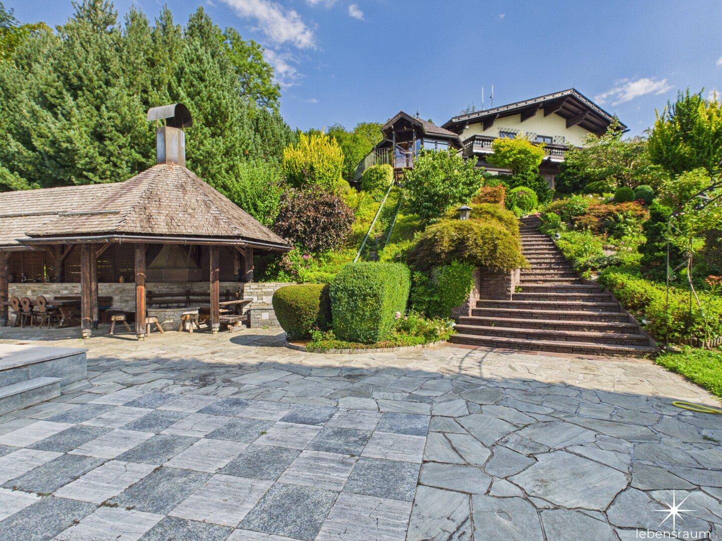 Weitläufiger Terrassengarten mit Steintreppen, üppiger Bepflanzung und Außenküche.