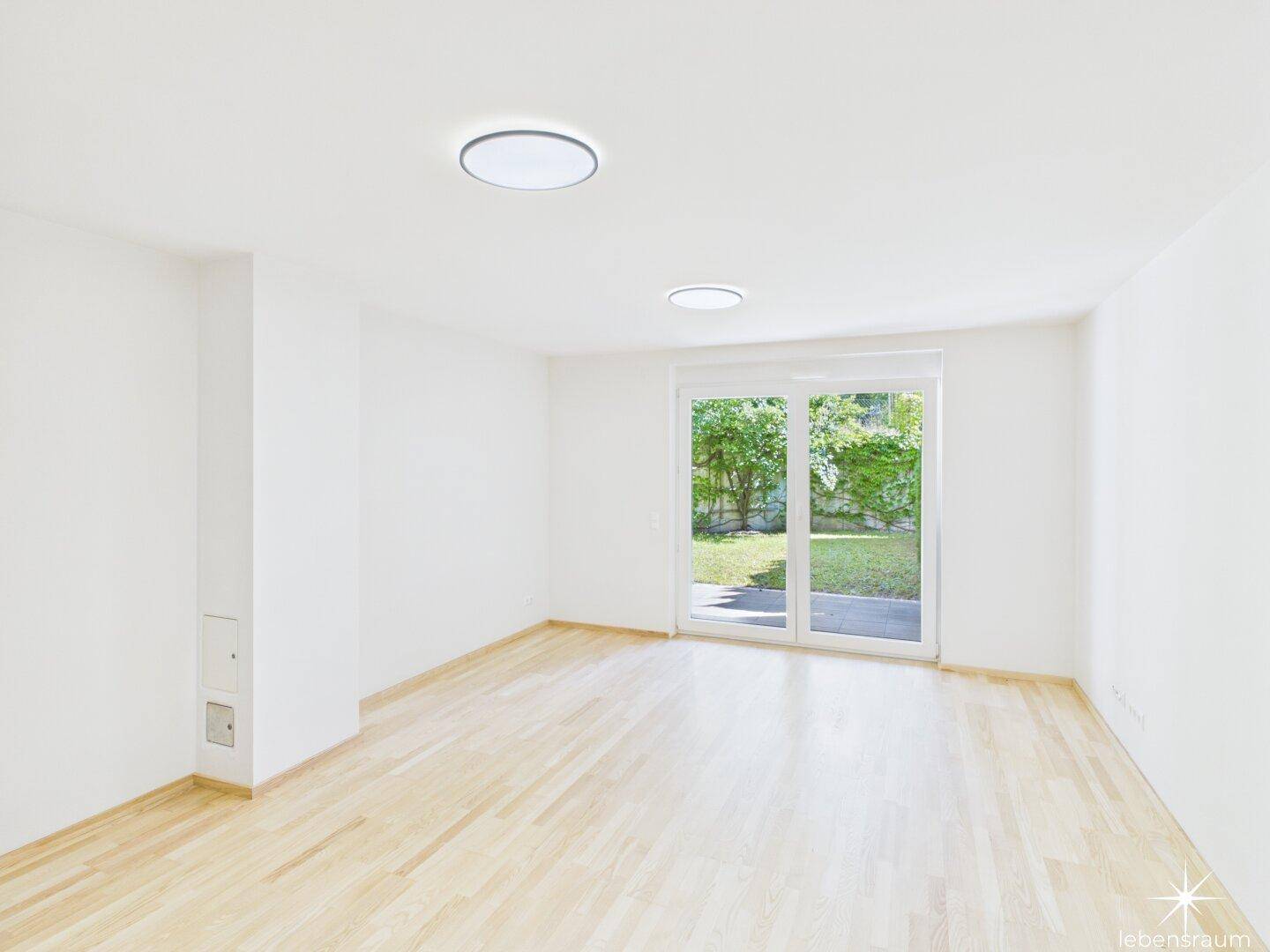 Heller, leerer Raum mit Holzboden und Zugang zum Garten durch große Glastüren.