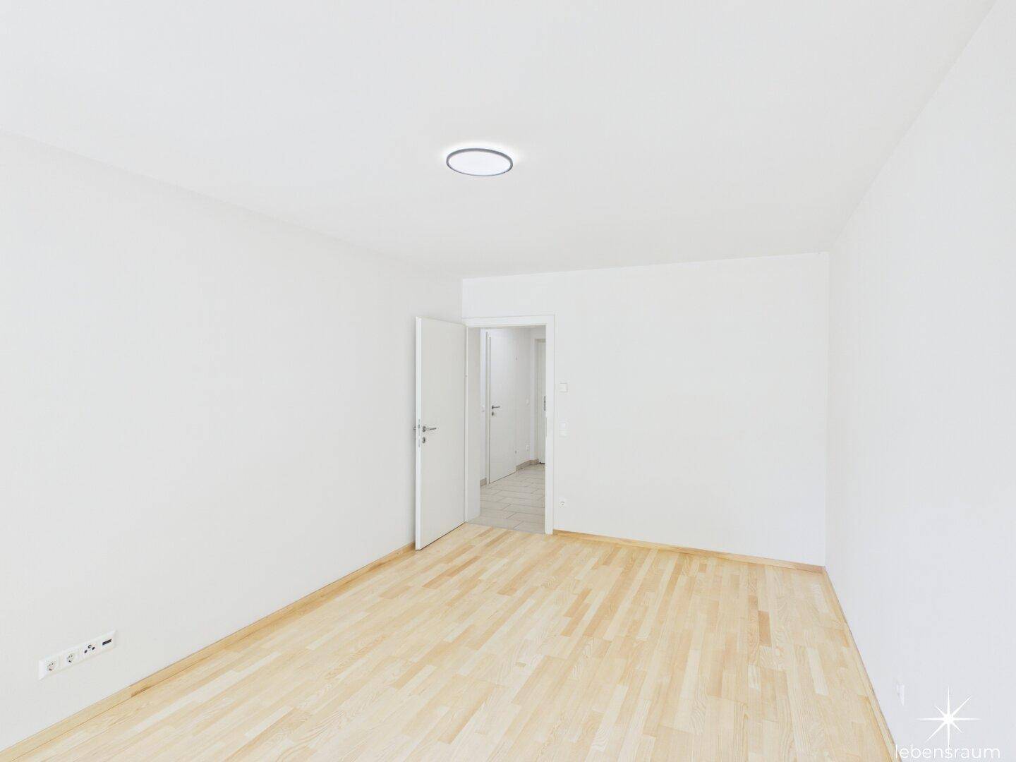 Leeres Schlafzimmer mit hellem Holzboden und weiß gestrichenen Wänden.