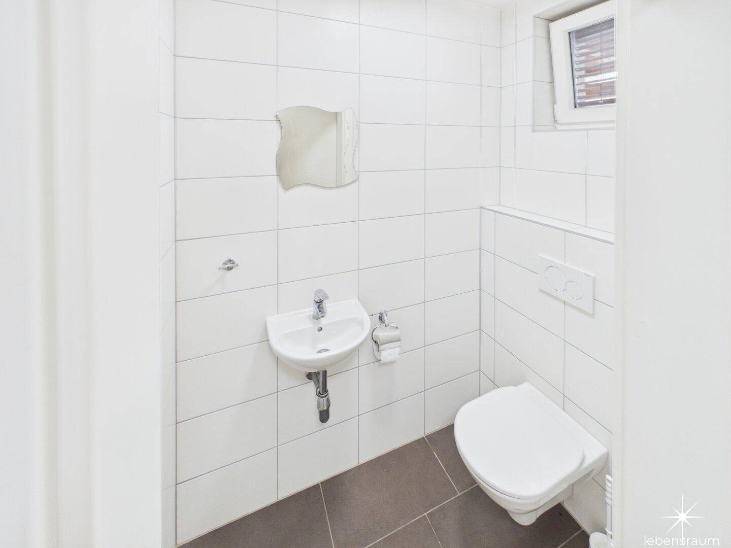 Kleines Gäste-WC mit weißen Fliesen, Waschbecken und wandhängendem WC.